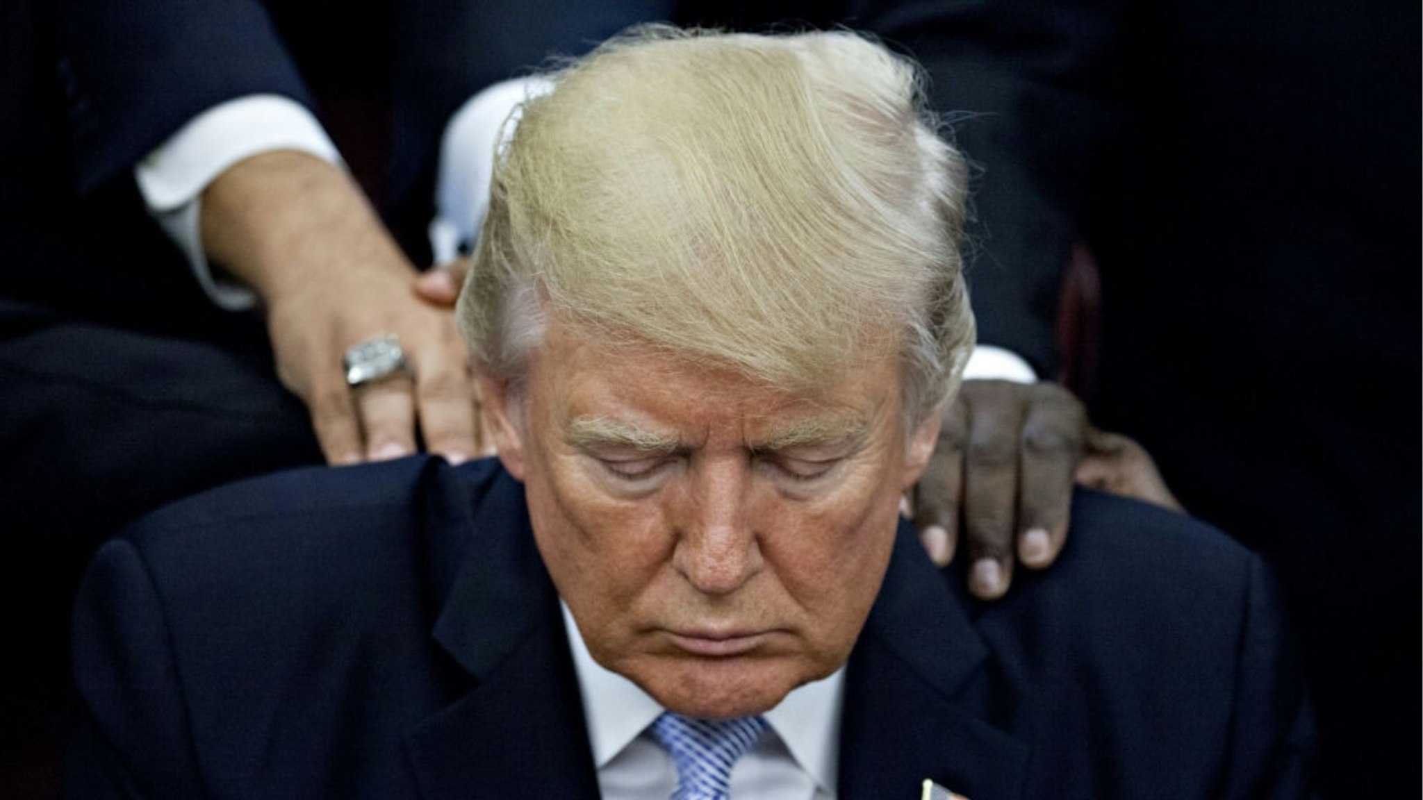 U.S. President Trump bows his head during a prayer while surrounded by faith leaders and evangelical ministers after signing a proclamation declaring a day of prayer in the Oval Office of the White House in Washington, D.C., U.S., on Friday, Sept. 1, 2017