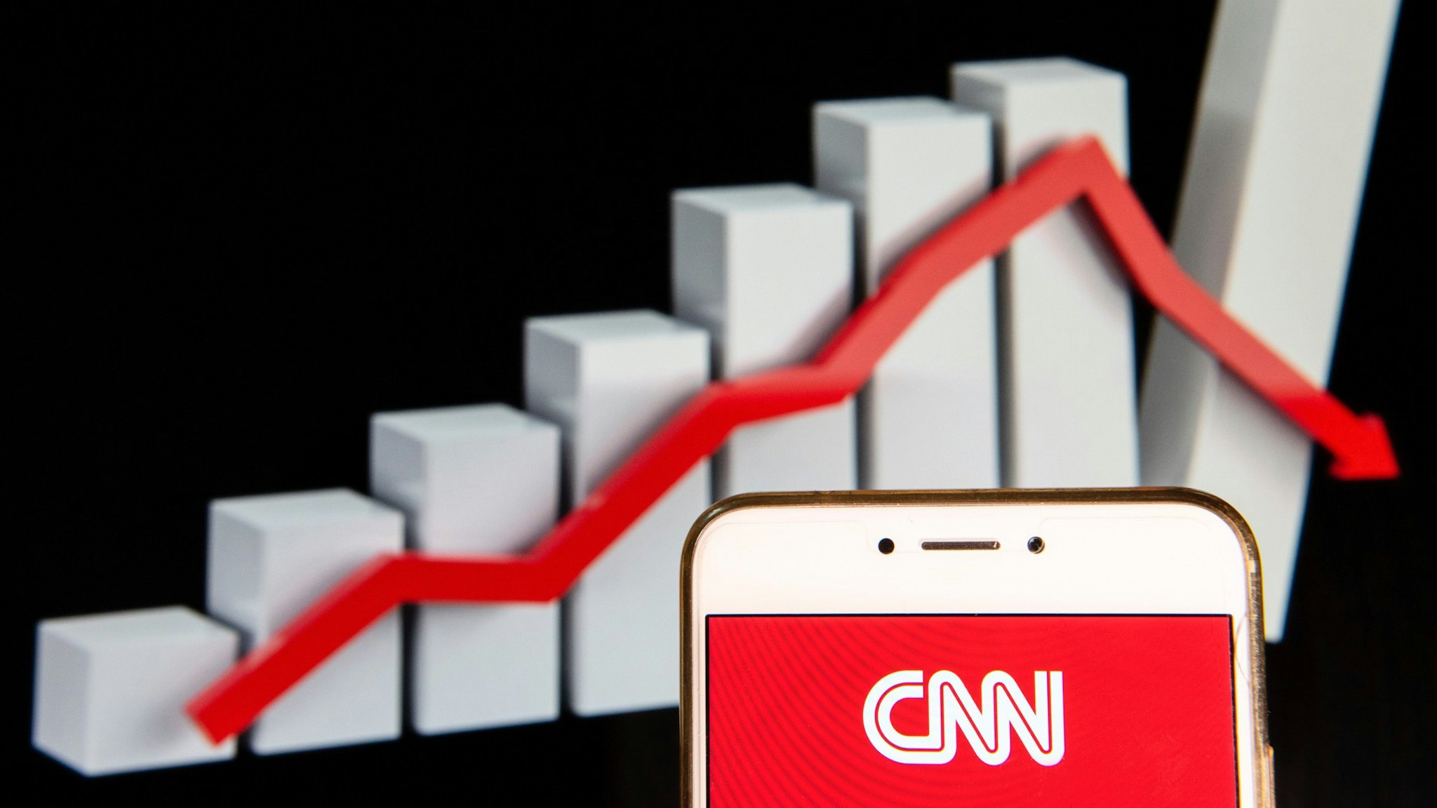 In this photo illustration, the CNN logo is seen displayed on an Android mobile device with a decline loses graph in the background.
