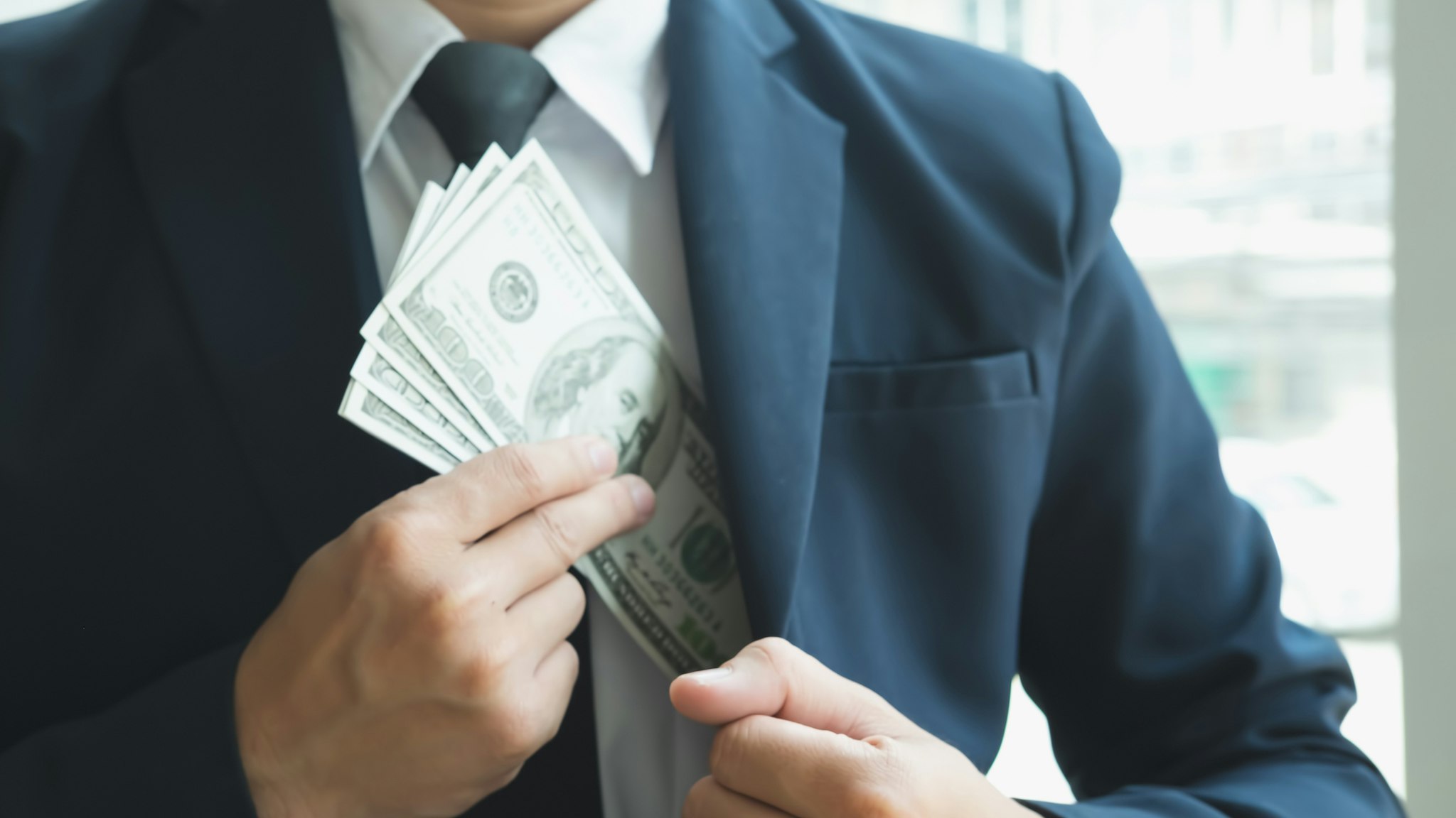 Midsection Of Businessman Putting Money Into Pocket