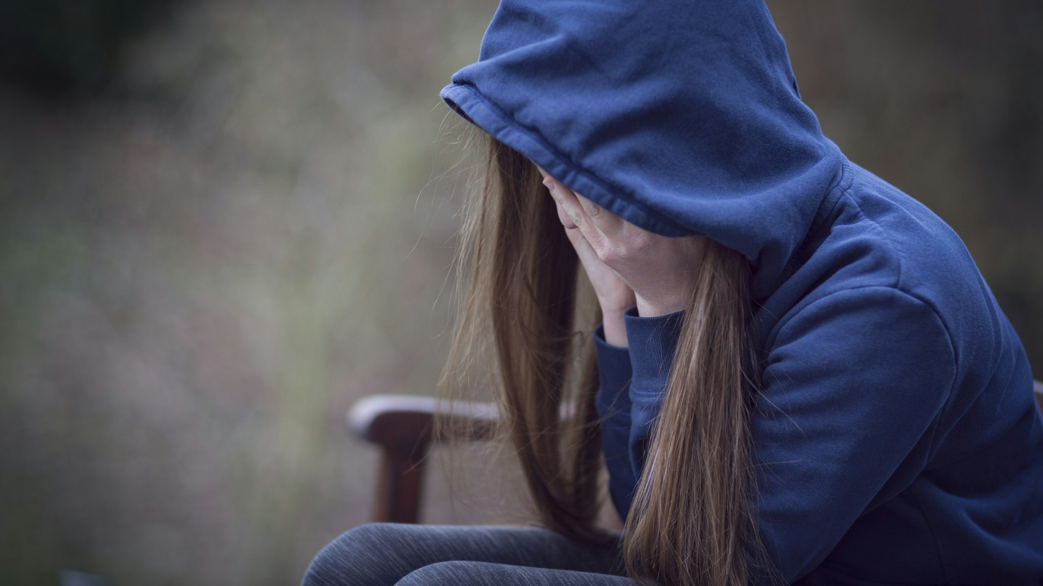 Teenage girl in hooded top, with head in hands in despair - stock photo