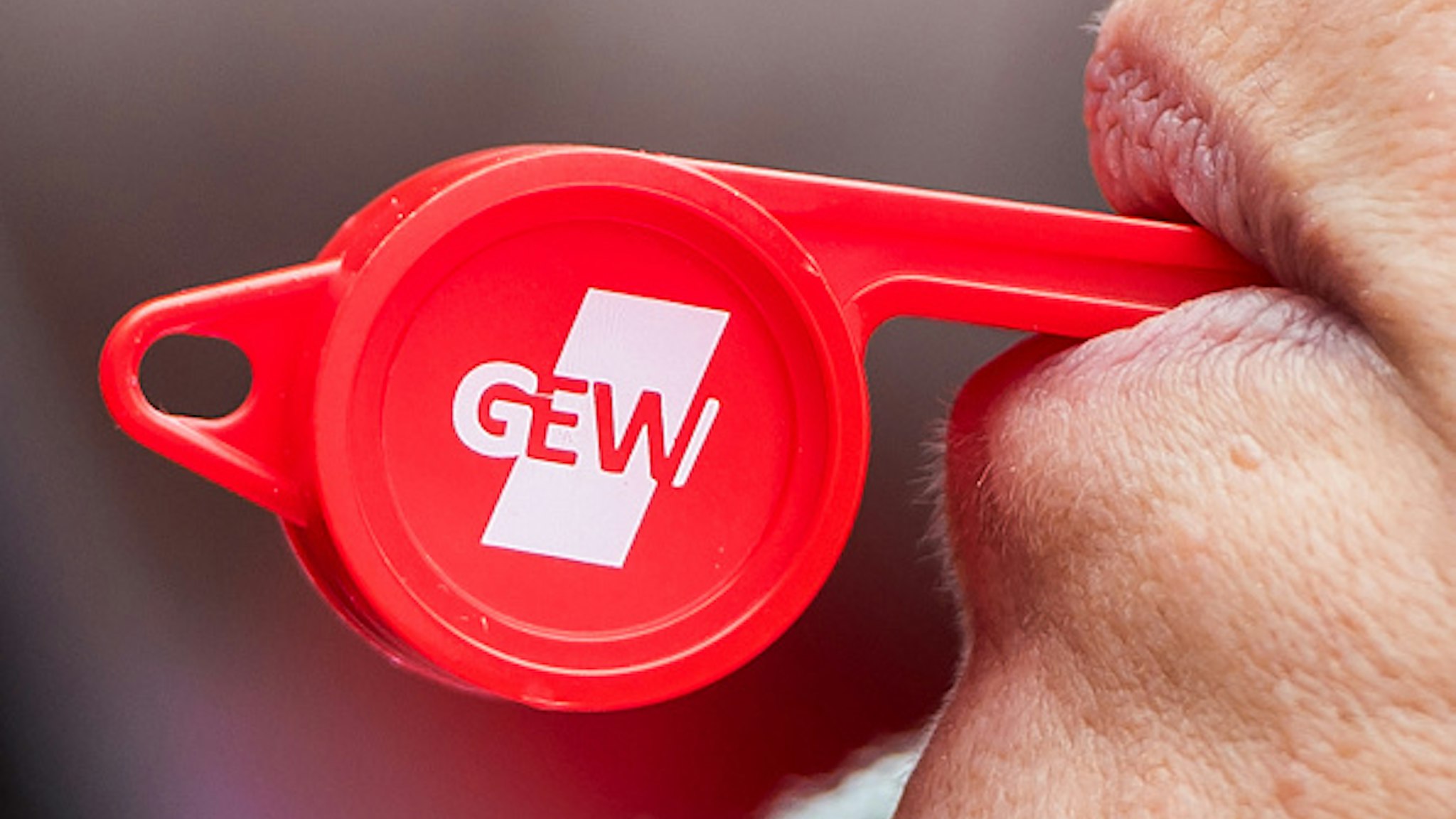 20 February 2019, Hamburg: A participant in a warning strike by collective bargaining employees at schools and universities in Hamburg stands in front of the tax authorities and blows a whistle with the logo of the GEW trade union. In the wage dispute in the public sector, the unions demand six percent more money, but at least 200 euros more per month.