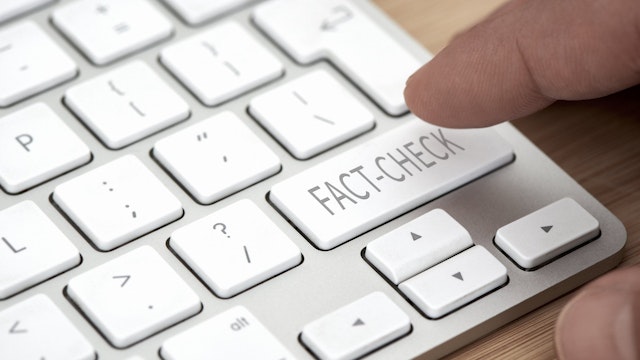 Finger about to press a key labeled "fact check" on a computer keyboard.