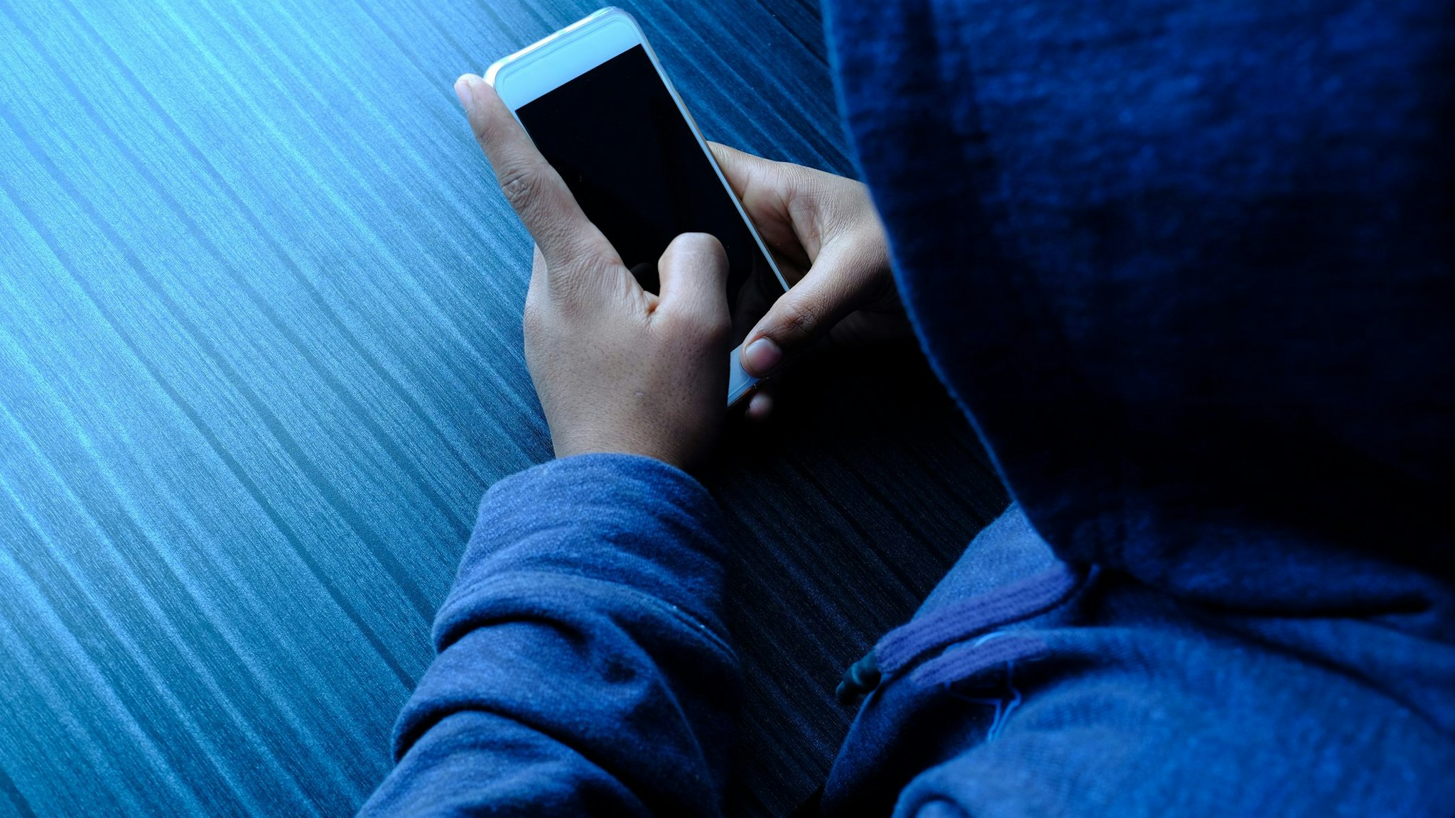 hooded cyber hacker stealing personal data using phone