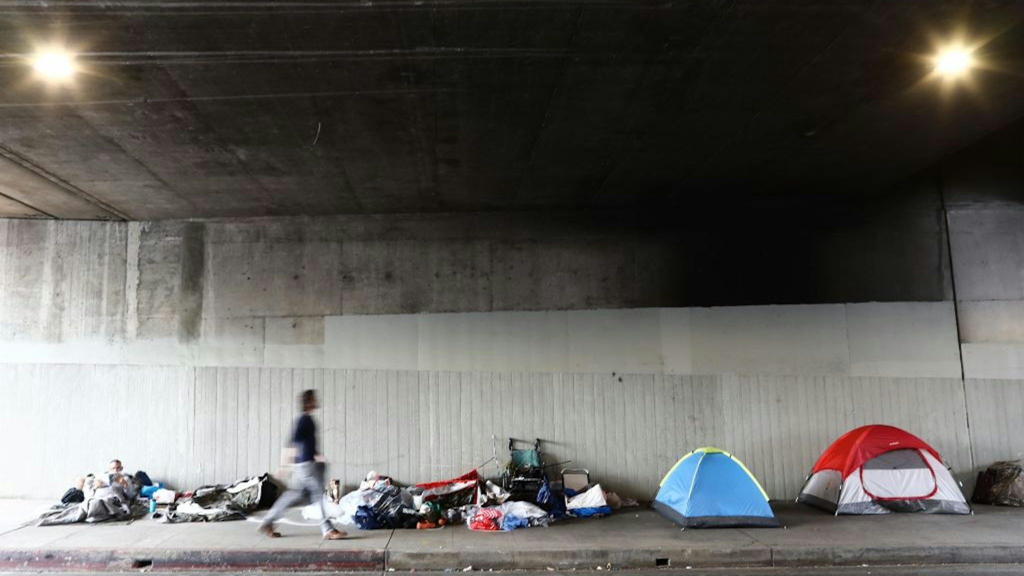 LOS ANGELES, CALIFORNIA - JUNE 05: A man walks past a homeless encampment beneath an overpass on June 5, 2019 in Los Angeles, California. The homeless population count in Los Angeles County leaped 12 percent in the past year to almost 59,000, according to officials.