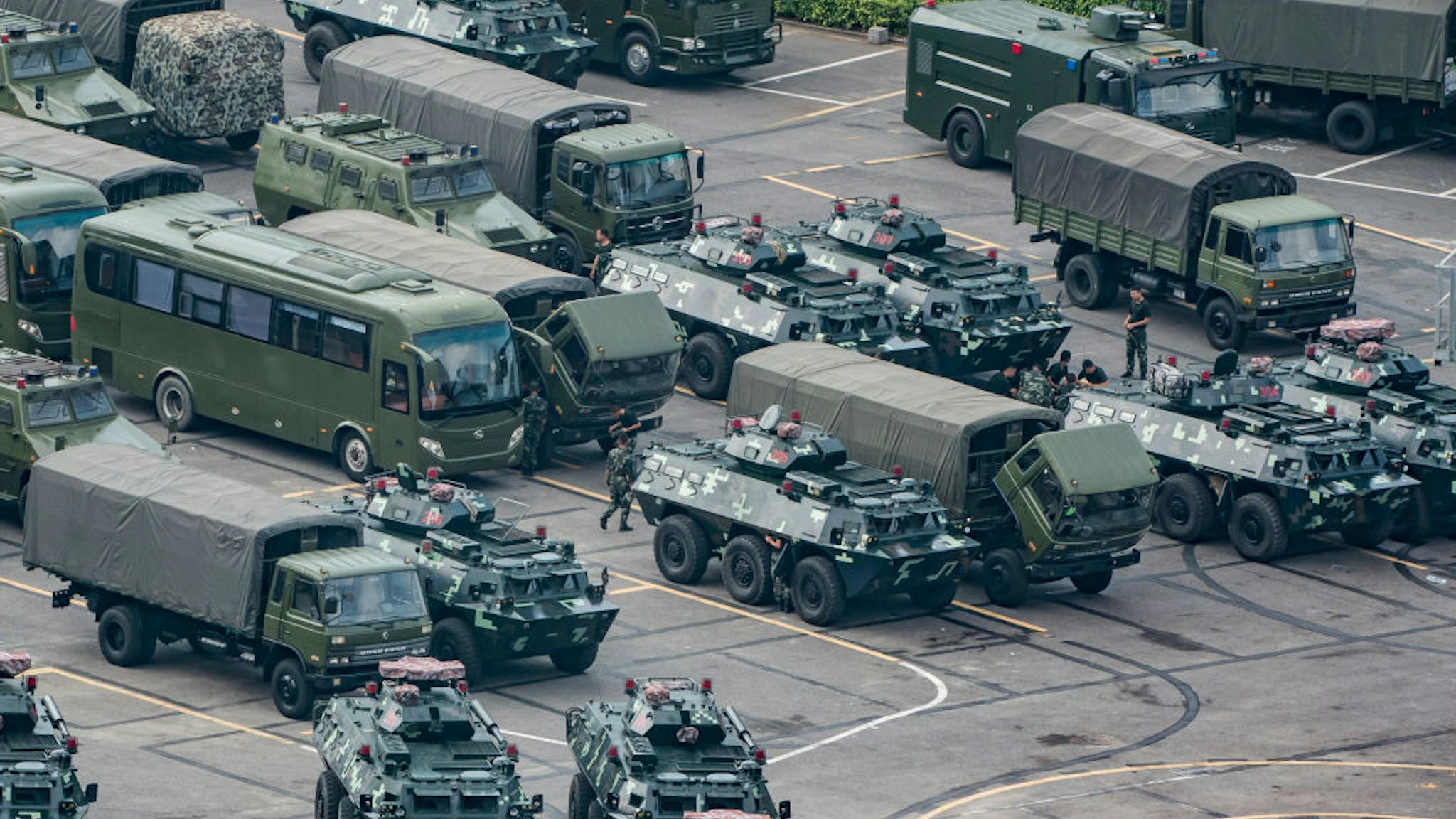 SHENZHEN, CHINA - AUGUST 16: Chinese military personnel maintain trucks and armoured personnel vehicles parked outside the Shenzhen Bay stadium on August 16, 2019 in Shenzhen, China. Pro-democracy protesters have continued rallies on the streets of Hong Kong against a controversial extradition bill since 9 June as the city plunged into crisis after waves of demonstrations and several violent clashes. Hong Kong's Chief Executive Carrie Lam apologized for introducing the bill and declared it "dead", however protesters have continued to draw large crowds with demands for Lam's resignation and completely withdraw the bill.