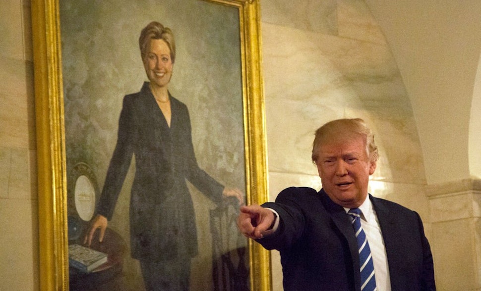 U.S. President Donald Trump walks in a corridor of the White House to greet visitors, while a portrait of Hillary Clinton hangs on the wall, March 7, 2017 in Washington, DC .