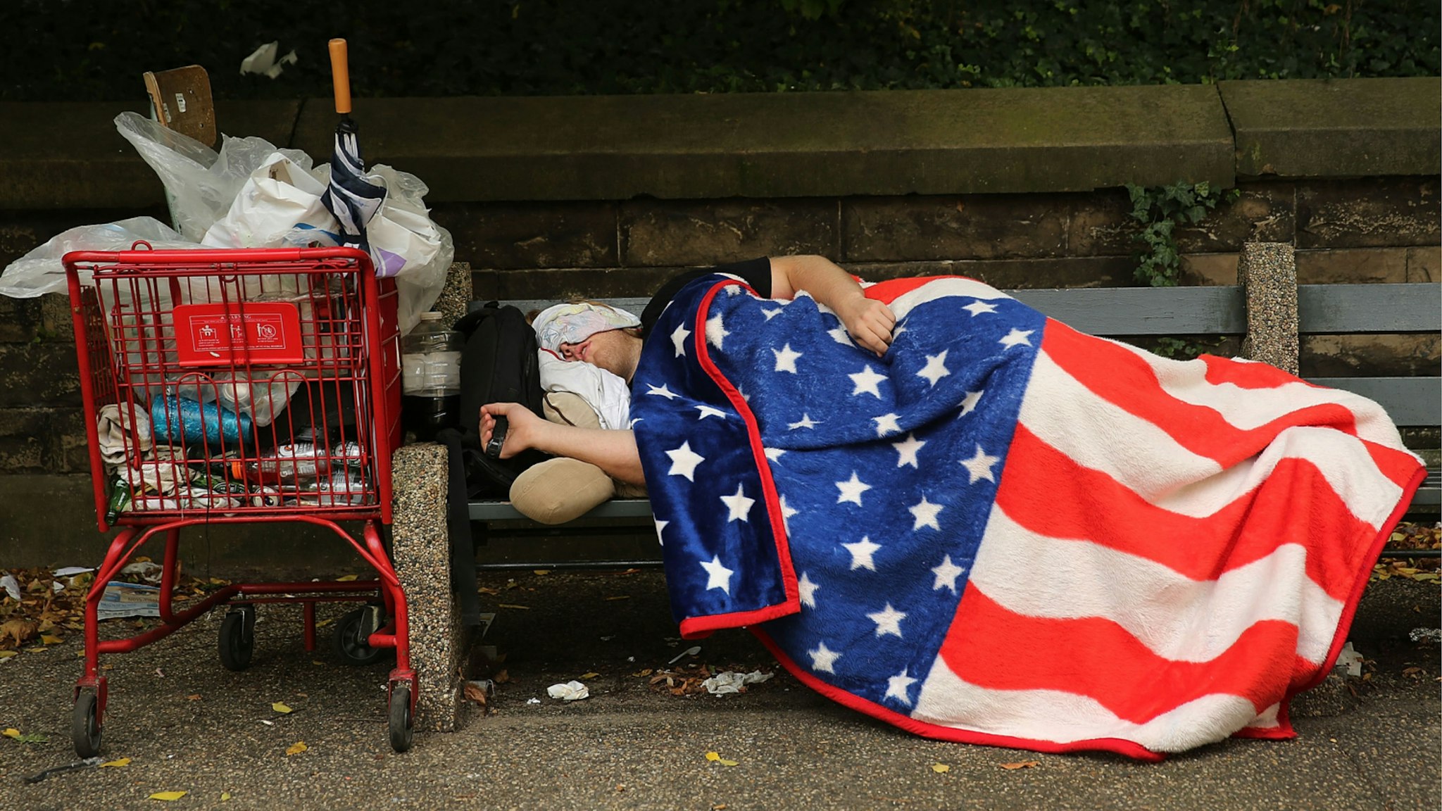 A homeless man sleeps under an American Flag blanket on a park bench on September 10, 2013 in the Brooklyn borough of New York City.
