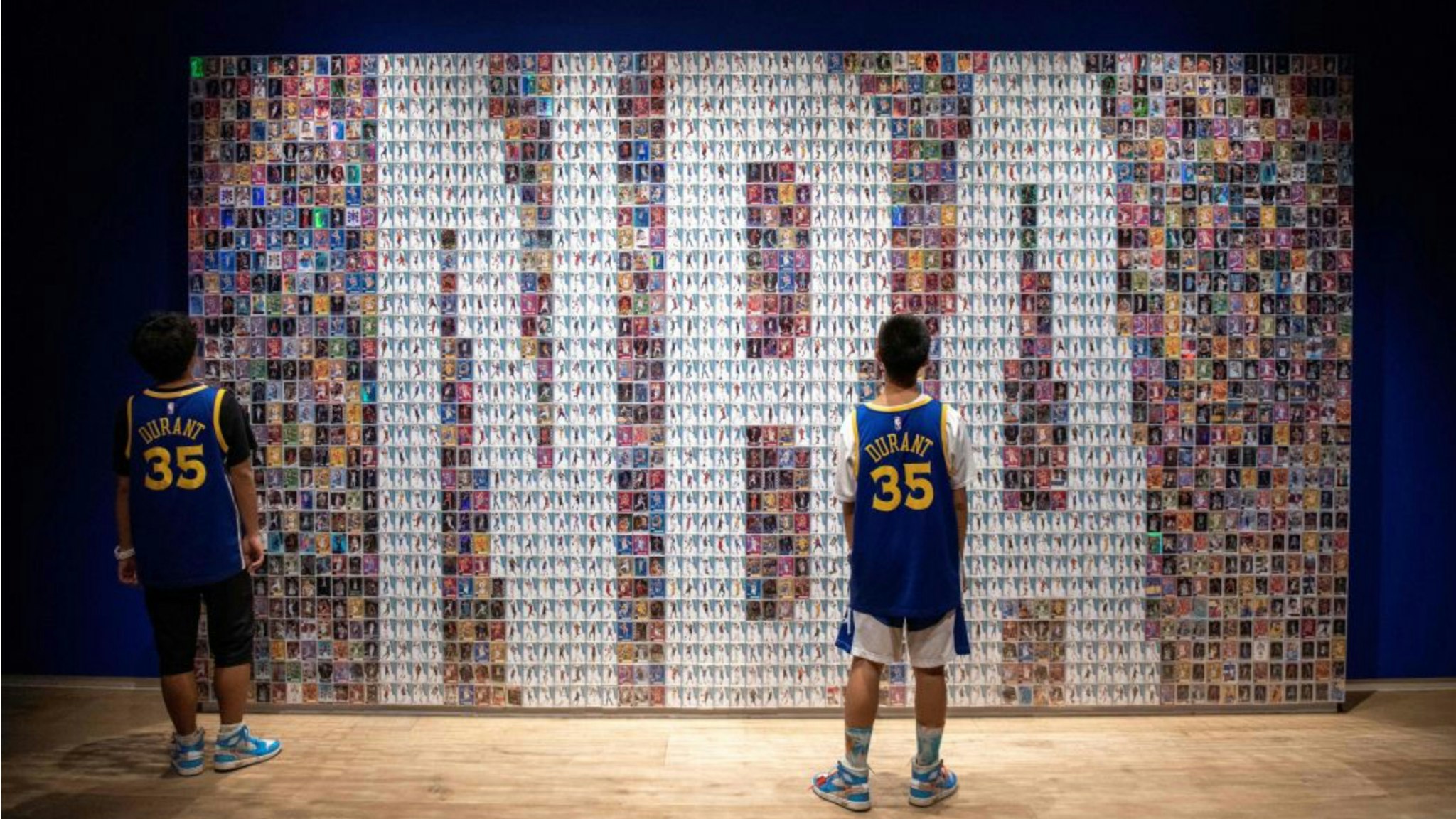Two Chinese youths stand in front of a wall displaying basketball trading cards at the NBA exhibition in Beijing on August 19, 2019. - The Basketball world cup will be held from August 31 to September 15 2019 in China.