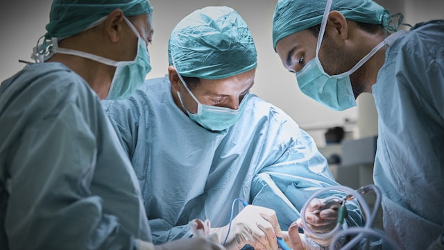 Plastic surgeons operating patient for breast implant. Team of doctors are in scrubs at operating room. They are at hospital.