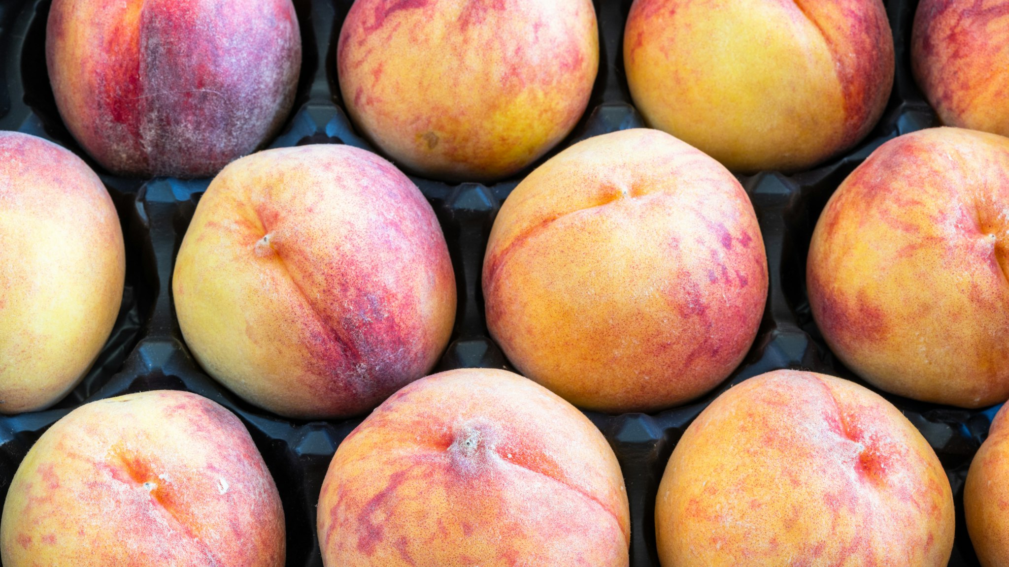 Large peaches forming a pattern inside of a box. Peaches are a healthy food because they are rich in potassium plus vitamins A, C, and E.