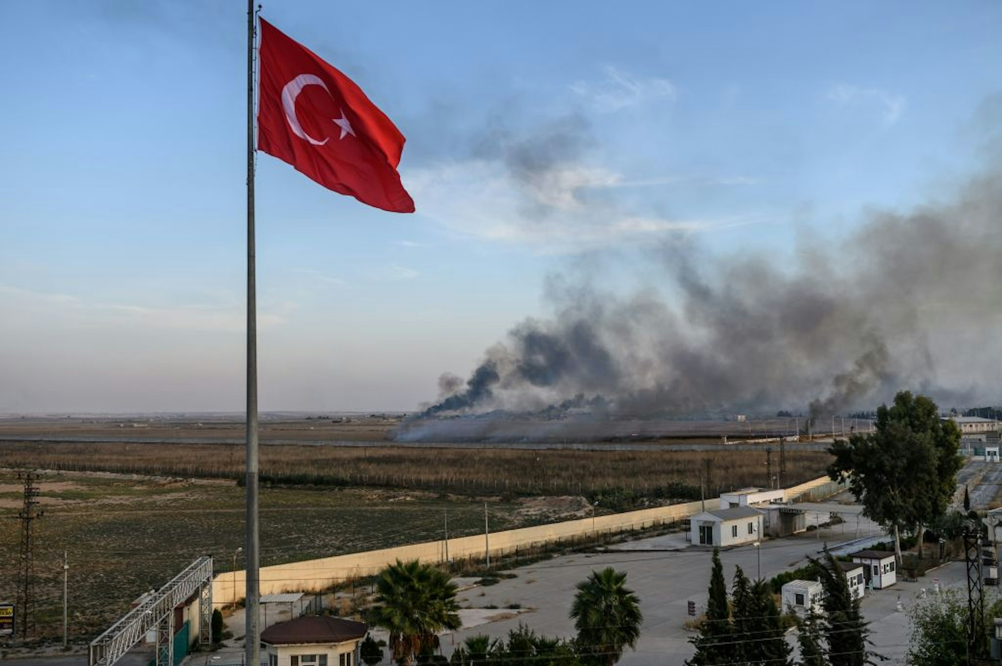 Smoke rises from the Syrian town of Tal Abyad, in a picture taken from the Turkish side of the border where the Turkish flag is seen in Akcakale on October 10, 2019, on the second day of Turkey's military operation against Kurdish forces.