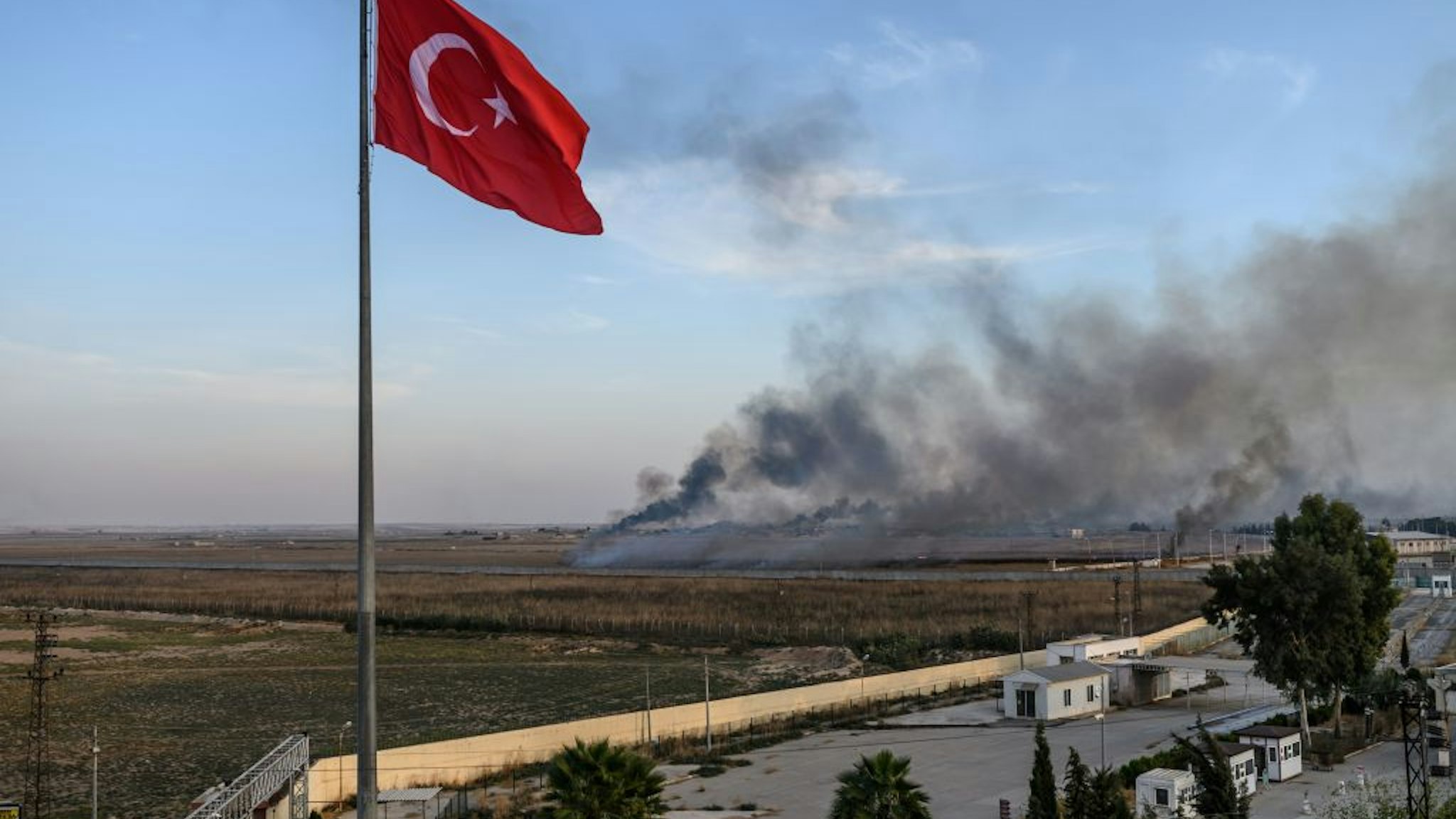 Smoke rises from the Syrian town of Tal Abyad, in a picture taken from the Turkish side of the border where the Turkish flag is seen in Akcakale on October 10, 2019, on the second day of Turkey's military operation against Kurdish forces.