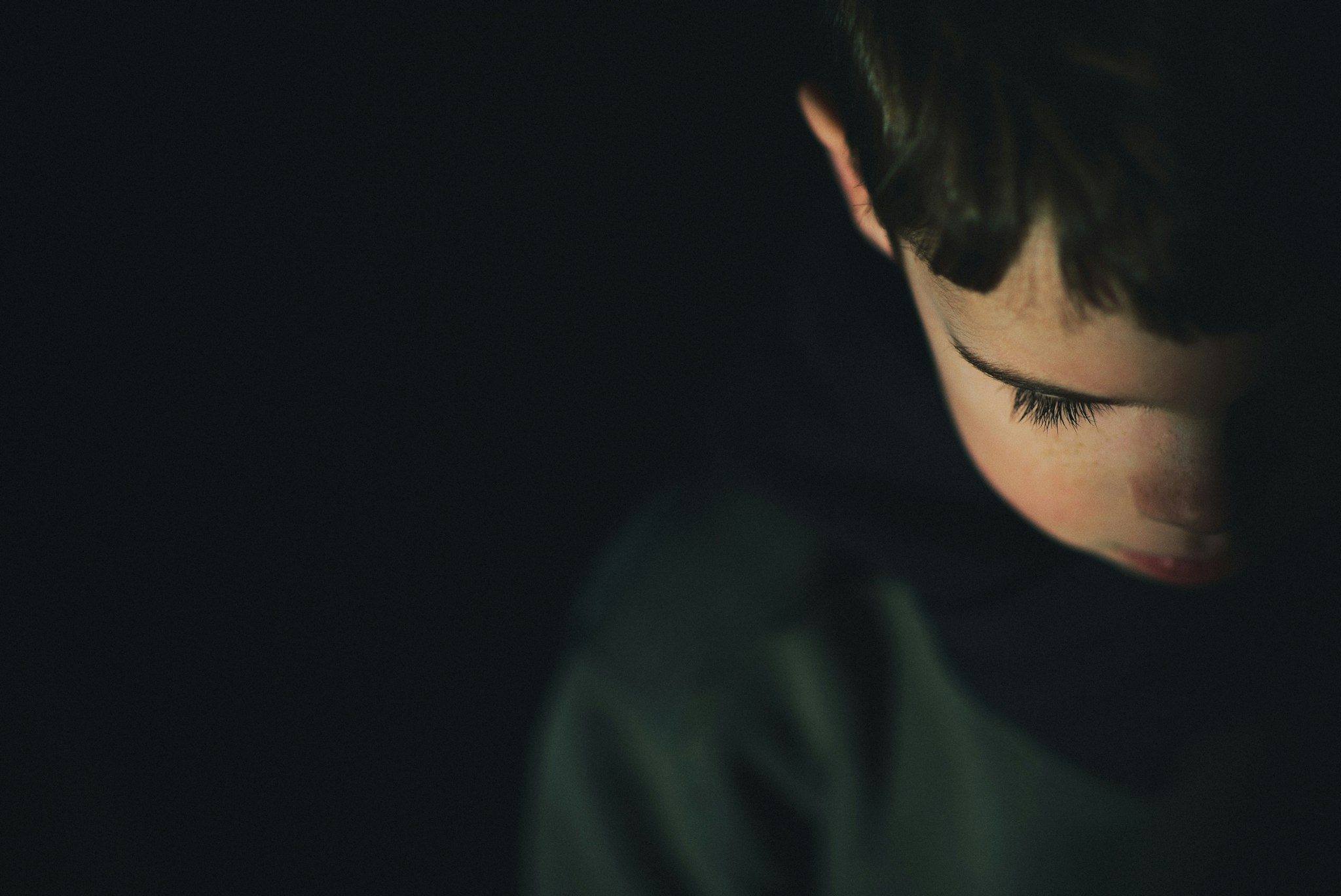Close up of young boy looking down on dark background.
