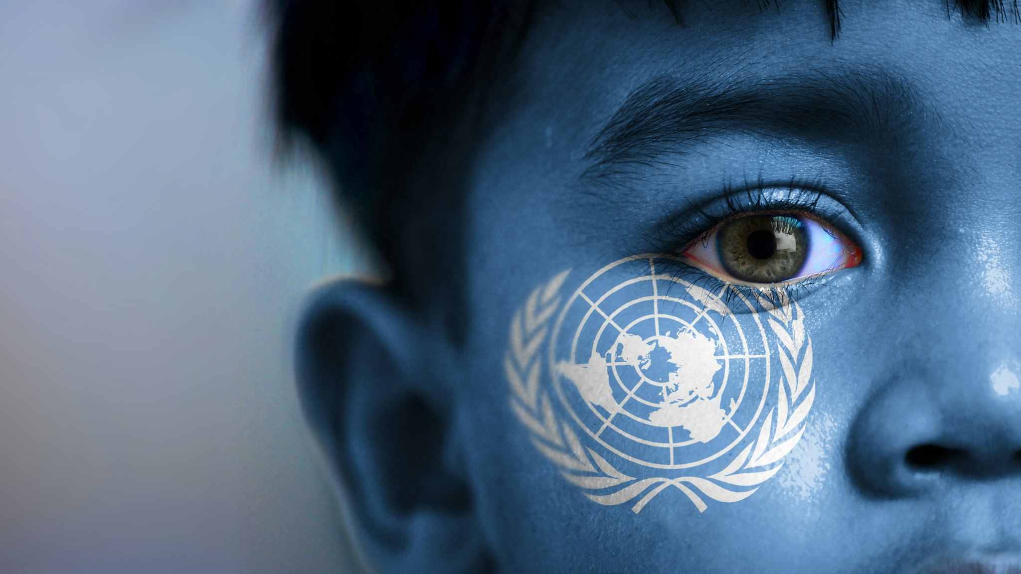 Boy's face, looking at camera, cropped view with digitally placed United Nations flag on his face.