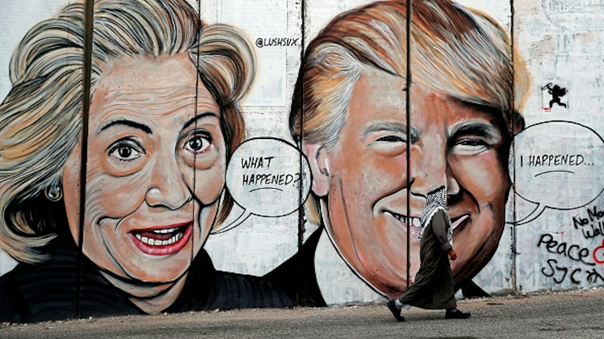 TOPSHOT - A Palestinian man walks past a newly sprayed graffiti depicting US presidential candidate Hillary Clinton and US President Donald Trump on the controversial Israeli separation wall separating the West Bank town of Bethlehem from Jerusalem on October 30, 2017.