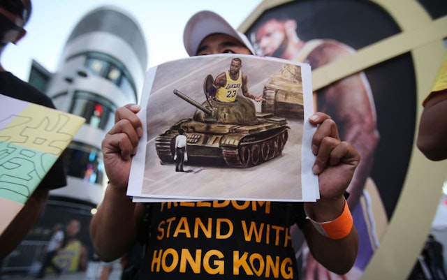A pro-Hong Kong activist holds an image depicting LeBron James aboard a Chinese tank in Tiananmen Square before the Los Angeles Lakers season opening game against the LA Clippers outside Staples Center on October 22, 2019 in Los Angeles, California. Activists also printed at least 10,000 pro-Hong Kong t-shirts to hand out to those attending the game and encouraged them to wear the free shirts as a form of peaceful protest against China amidst Chinese censorship of NBA games. (Photo by Mario Tama/Getty Images)