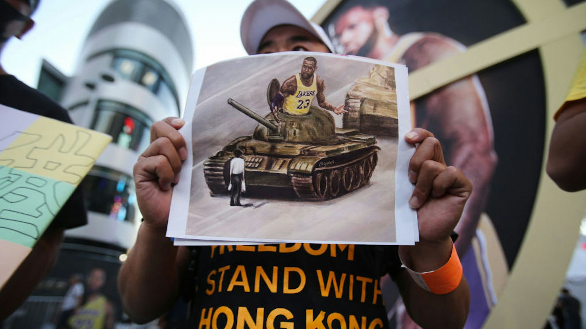 A pro-Hong Kong activist holds an image depicting LeBron James aboard a Chinese tank in Tiananmen Square before the Los Angeles Lakers season opening game against the LA Clippers outside Staples Center on October 22, 2019 in Los Angeles, California. Activists also printed at least 10,000 pro-Hong Kong t-shirts to hand out to those attending the game and encouraged them to wear the free shirts as a form of peaceful protest against China amidst Chinese censorship of NBA games. (Photo by Mario Tama/Getty Images)