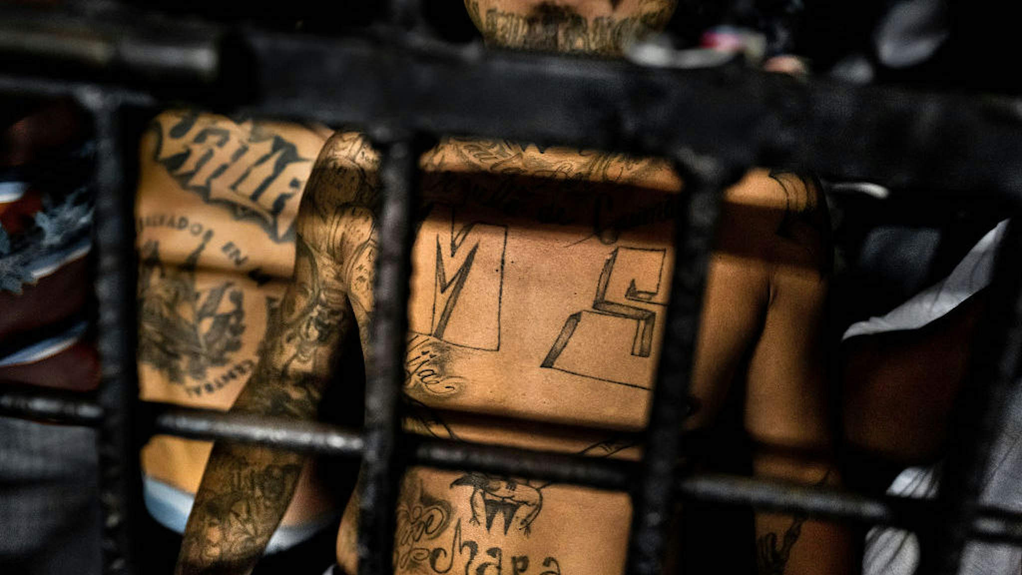 A member of the Mara Salvatrucha gang (MS-13) stands behind bars in a cell at a detention center on February 20, 2014 in San Salvador, El Salvador. Although the country's two major gangs reached a truce in 2012, the police holding cells currently house more than 3000 inmates, five times the official capacity. Partly because Mara gang members did not break with their criminal activities, partly because Salvadorean police still applies a controversial anti-gang law which allows to detain almost anyone for suspicion of gang membership. Accused young men are held in police detention centers where up to 25 inmates may share a cell of five square metres. In the dark overcrowded cages, under harsh and life-threatening conditions, suspected gang members wait for trial or for to be transported to a regular prison. (Photo by Jan Sochor/LatinContent/Getty Images)