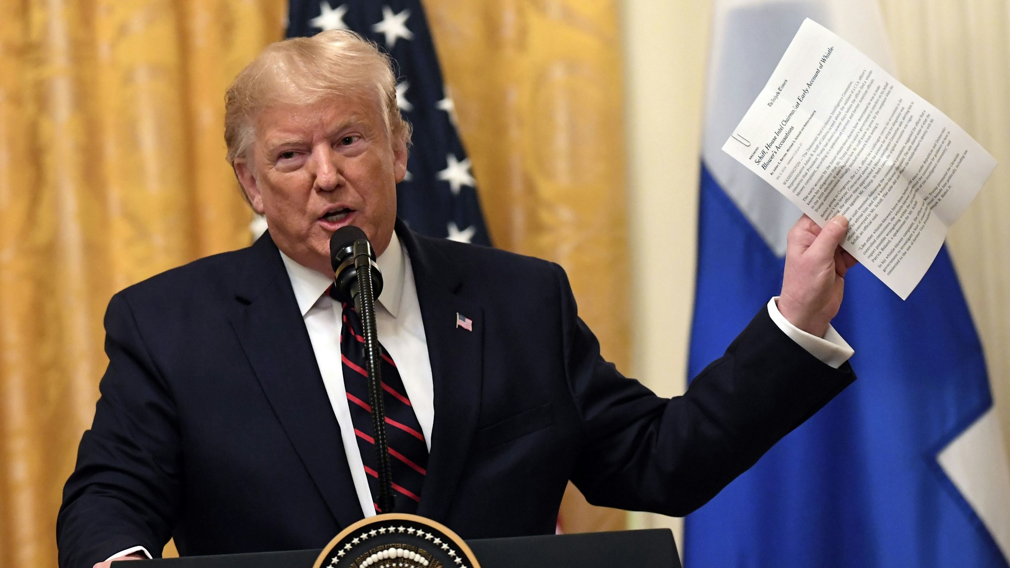 US President Donald Trump holds up a NYTimes report on House Intelligence Committee chairman Adam Schiff as he and Finnish President Sauli Niinisto(not shown) hold a joint press conference in the East Room of the White House in Washington, DC, on October 2, 2019.