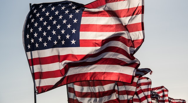 One main flag of the United States with many other flags, blowing in wind, with copy space