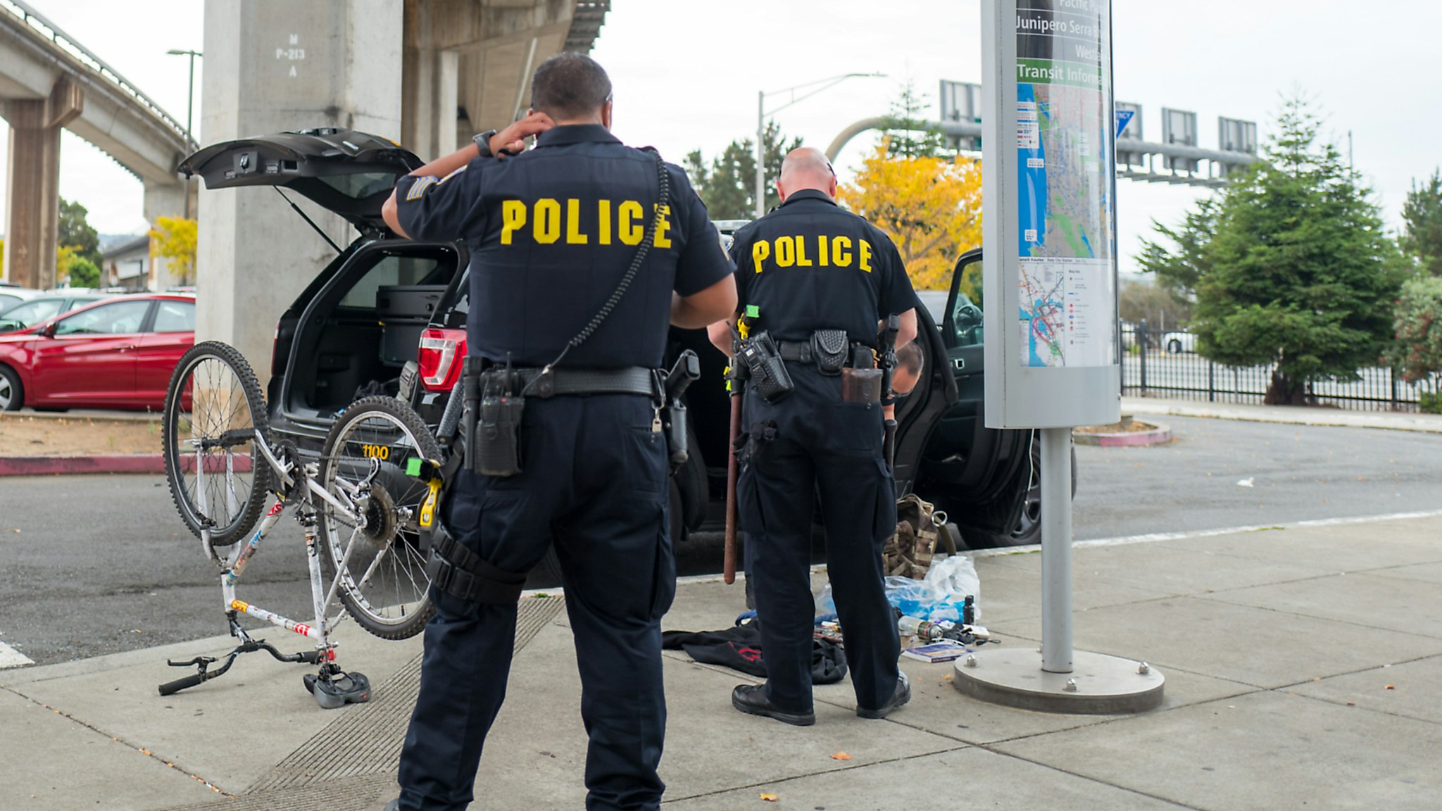 Two Bay Area Rapid Transit (BART) police officers are viewed from behind, with an overturned bicycle and bag with sorted contraband on the sidewalk in front of the officers, in the San Francisco Bay Area town of Daly City, California, November 3, 2017.