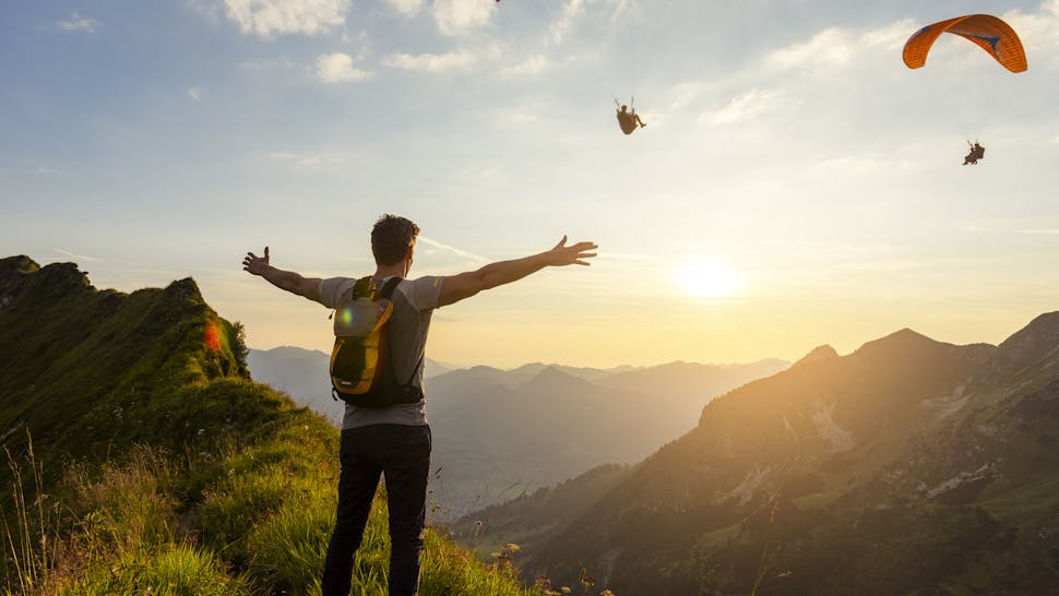 Hiking Germany, Bavaria, Oberstdorf, man on a hike in the mountains at sunset with paraglider in background