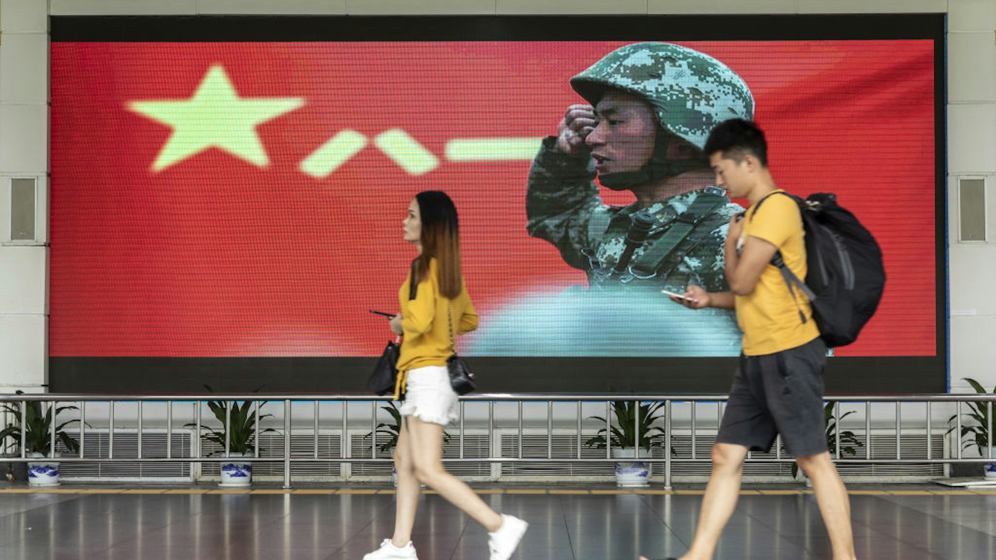 Pedestrians walk past an advertisement for the People's Liberation Army (PLA) on a screen near the Luohu border crossing in Shenzhen, China, on Thursday, Aug. 15, 2019.