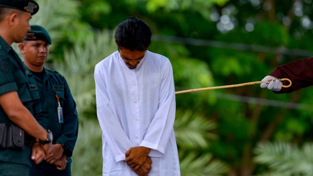 A man (C) is whipped in public by a member of the Sharia police after being charged with gambling in Banda Aceh on October 21, 2019.