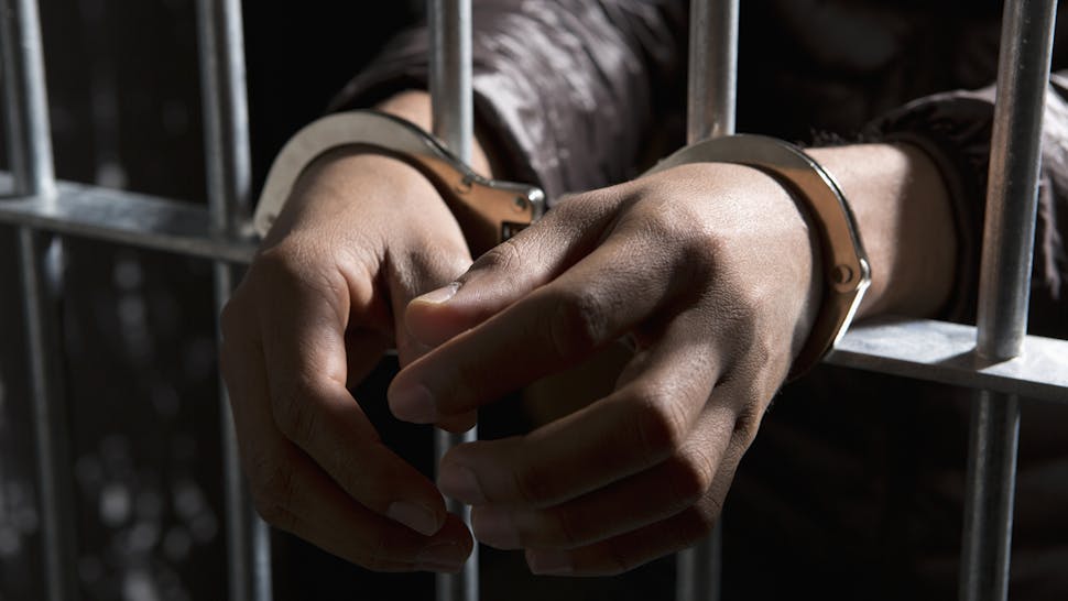 A prisoner behind bars with hands cuffed A prisoner behind bars with hands cuffed - stock photo