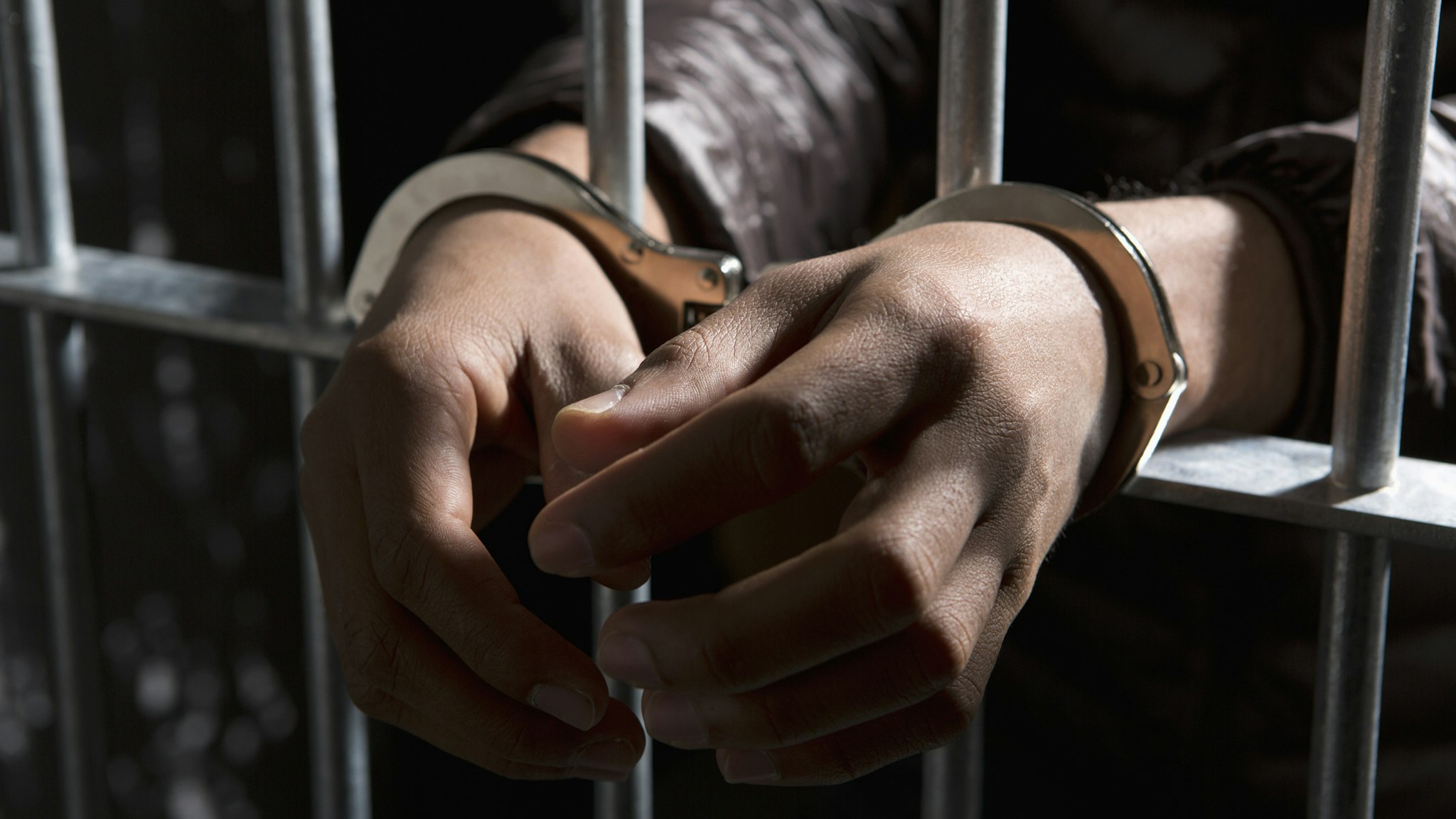 A prisoner behind bars with hands cuffed - stock photo