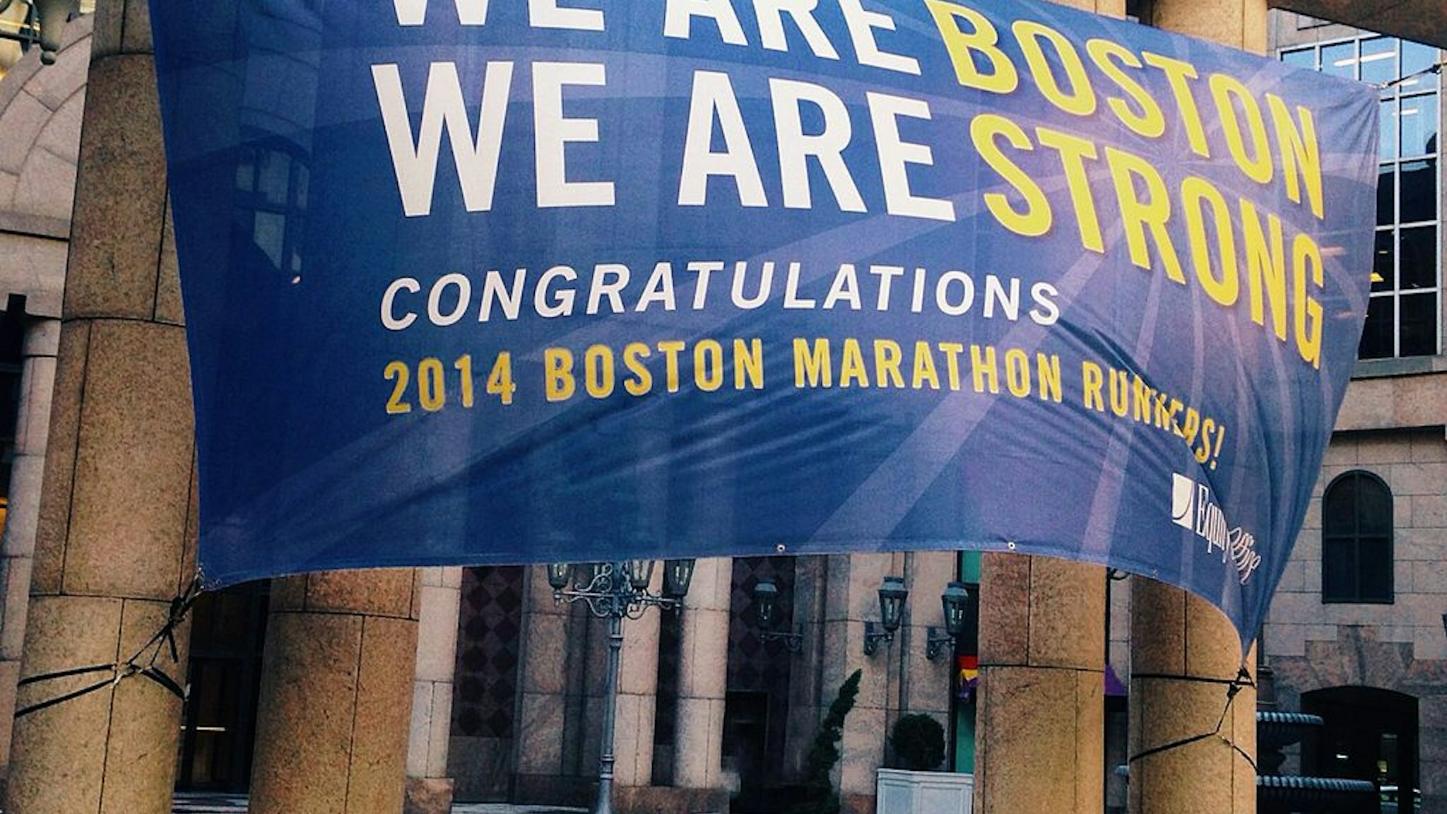 A banner honoring the 2014 Boston Marathon is strung from pillars on Boylston Street and strains in a strong wind.