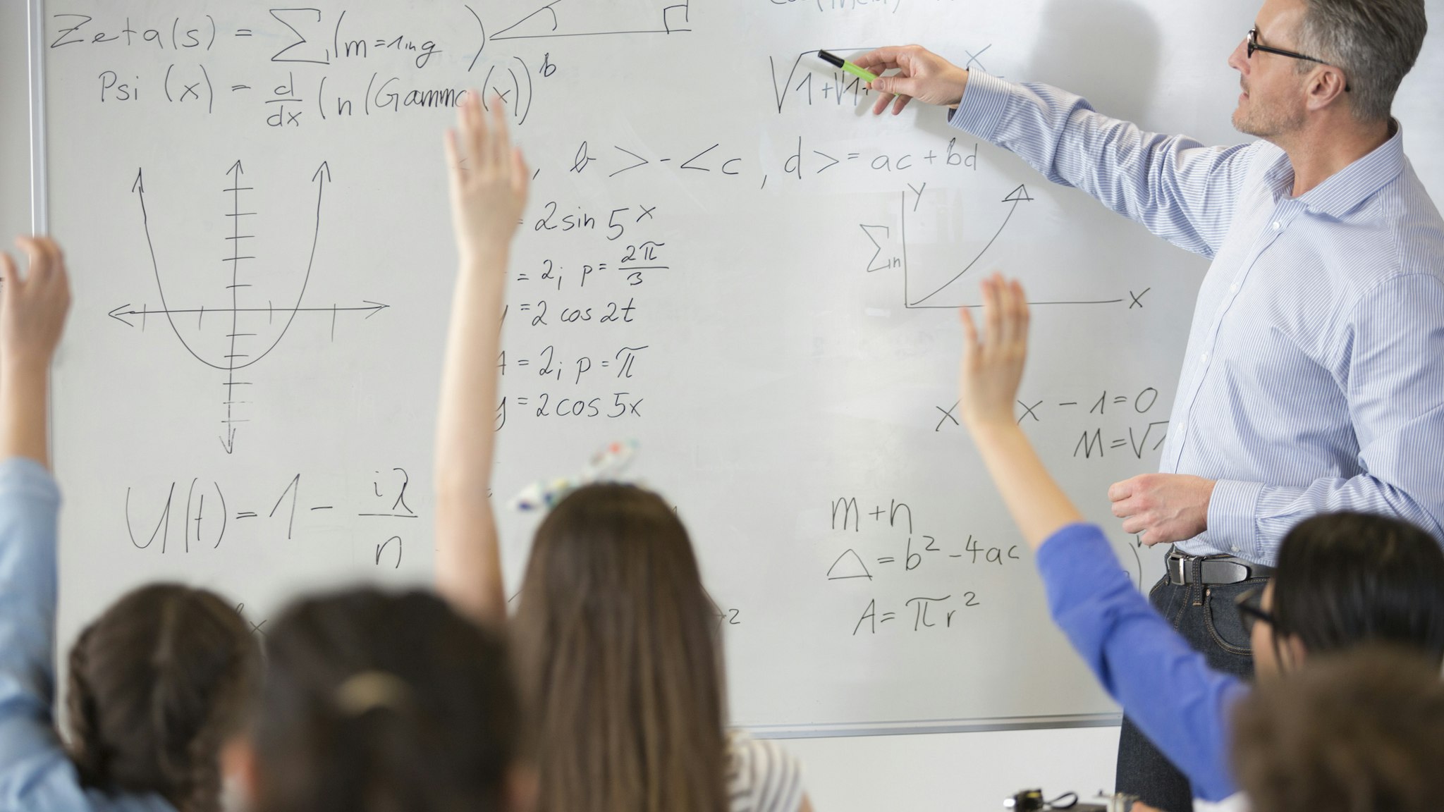 Male teacher leading physics lesson at whiteboard in classroom