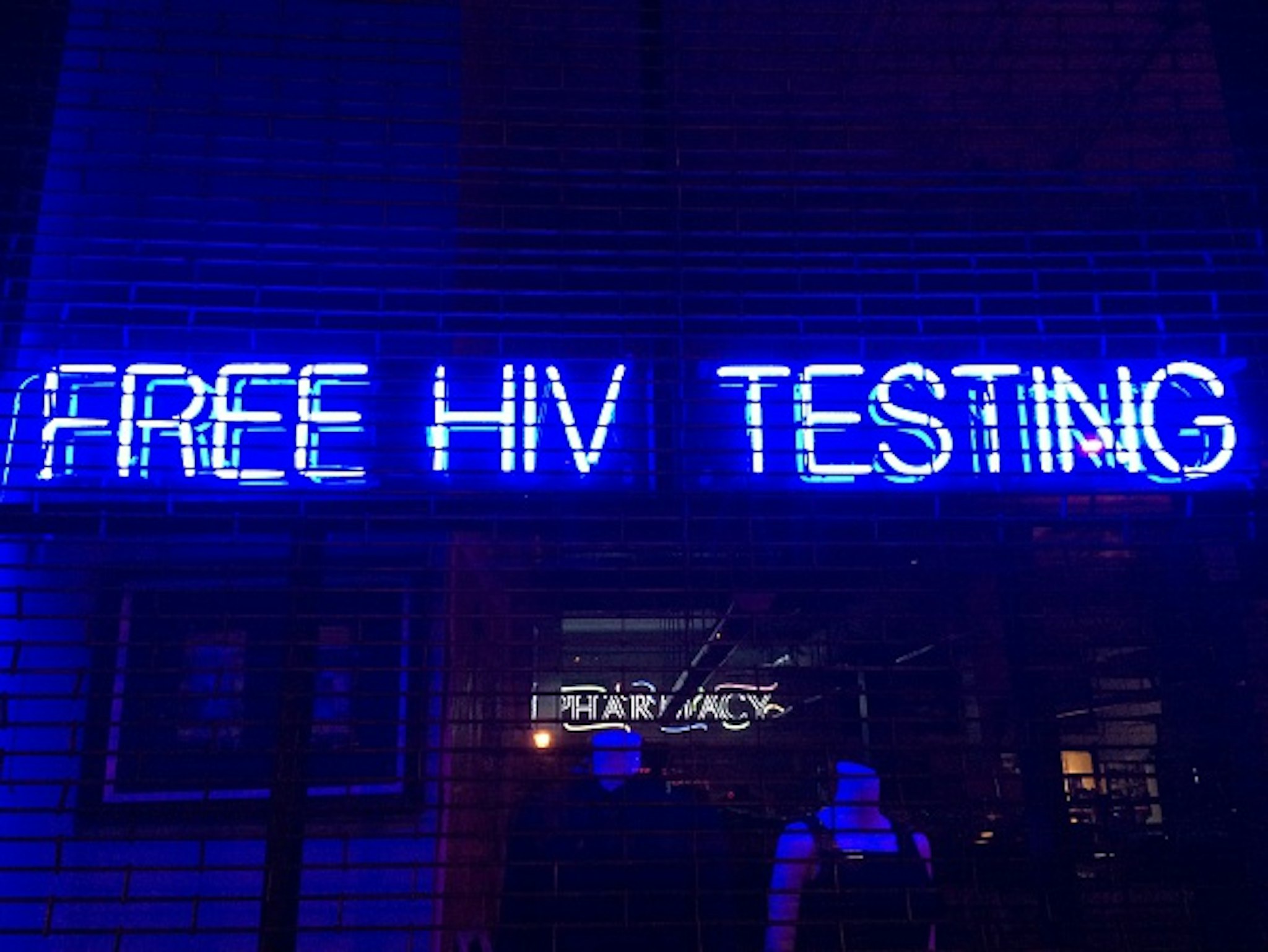 'Free HIV Testing' is spelled out in blue &amp; white neon letters hanging in a storefront window behind security gates in Boerum Hill, Brooklyn, NYC - March 9, 2015