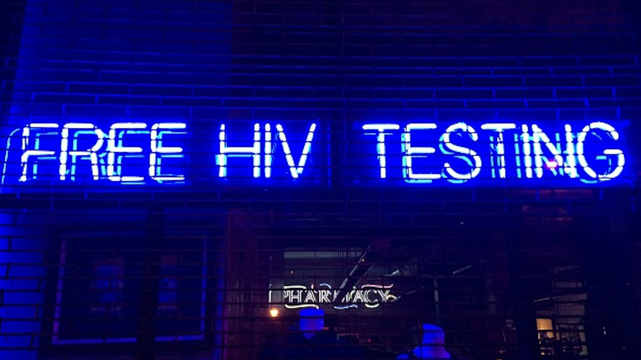 'Free HIV Testing' is spelled out in blue &amp; white neon letters hanging in a storefront window behind security gates in Boerum Hill, Brooklyn, NYC - March 9, 2015