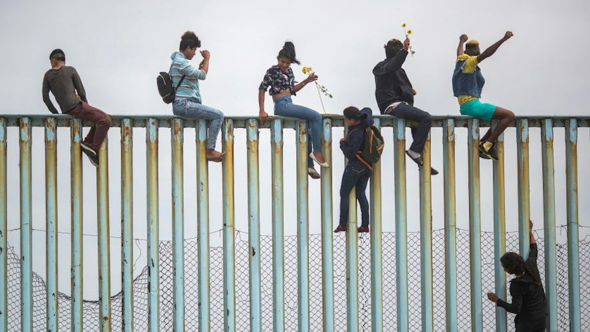People climb a section of border fence to look toward supporters in the U.S. as members of a caravan of Central American )