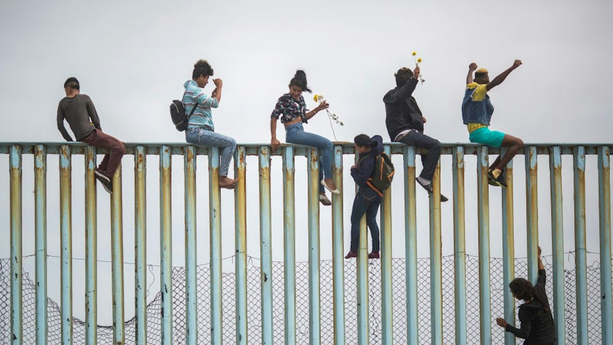 People climb a section of border fence to look toward supporters in the U.S. as members of a caravan of Central American asylum seekers arrive to a rally on April 29, 2018 in Tijuana, Baja California Norte, Mexico.