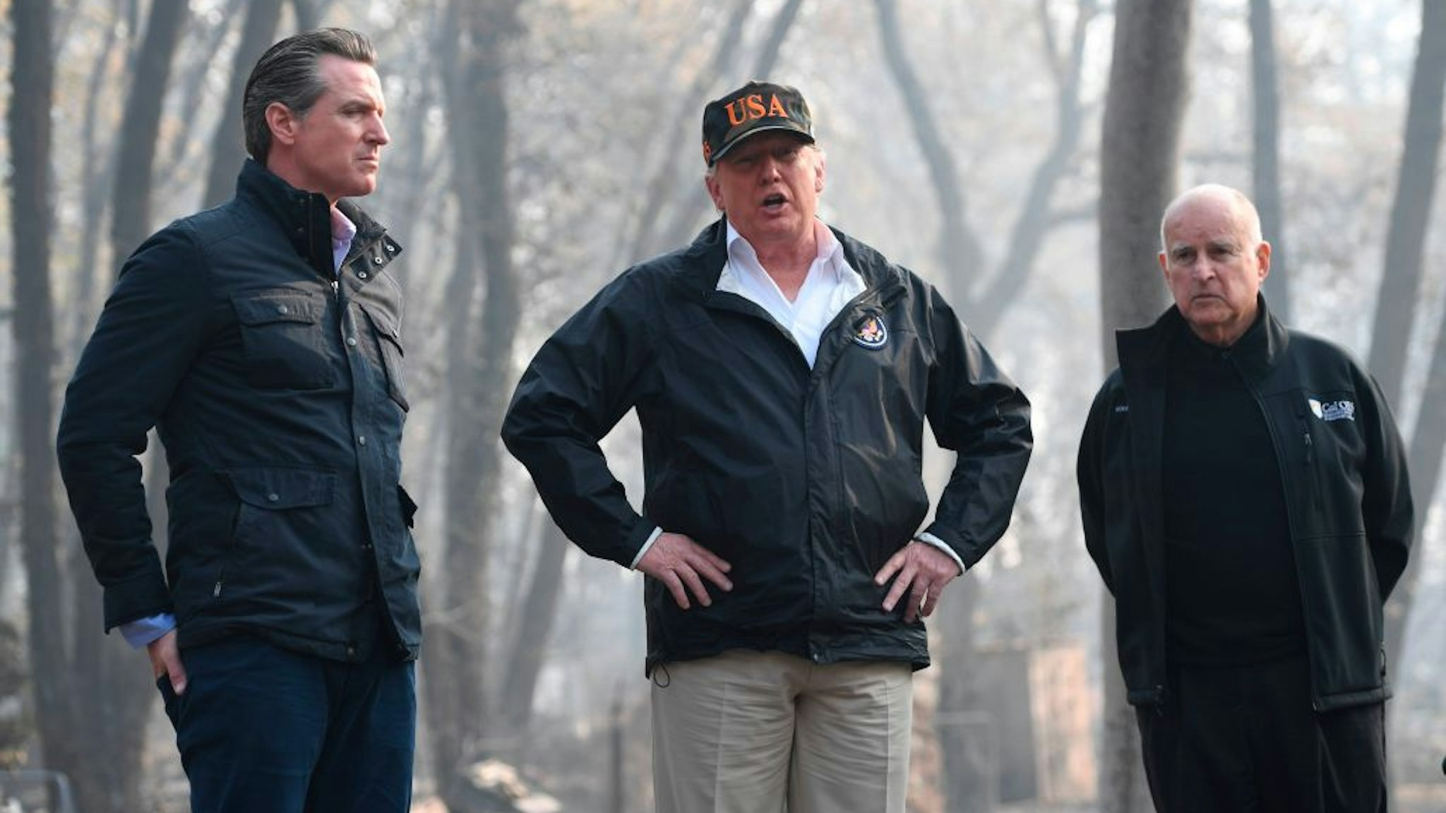 US President Donald Trump (C) looks on with Governor of California Jerry Brown (R) and Lieutenant Governor of California, Gavin Newsom, as they view damage from wildfires in Paradise, California on November 17, 2018. - President Donald Trump arrived in California to meet with officials, victims and the "unbelievably brave" firefighters there, as more than 1,000 people remain listed as missing in the worst-ever wildfire to hit the US state. (Photo by SAUL LOEB / AFP) (Photo credit should read SAUL LOEB/AFP via Getty Images)