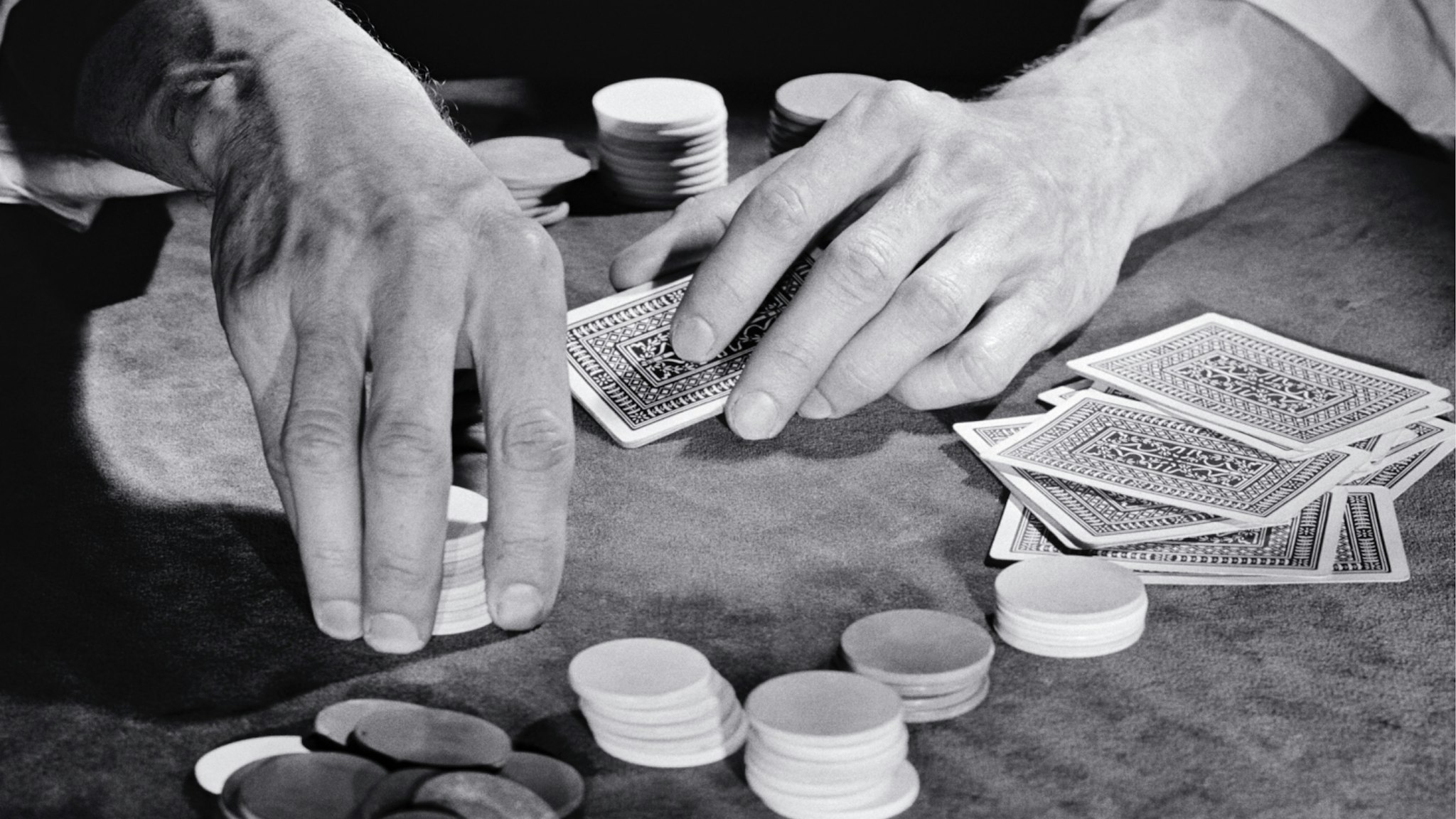1930s 1940s 1950s Man Hands Gambler Playing Game Of Cards Sitting At Poker Table Holding Chips About To Place Bet.