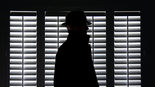 Silhouette of a man in hat against screen window.