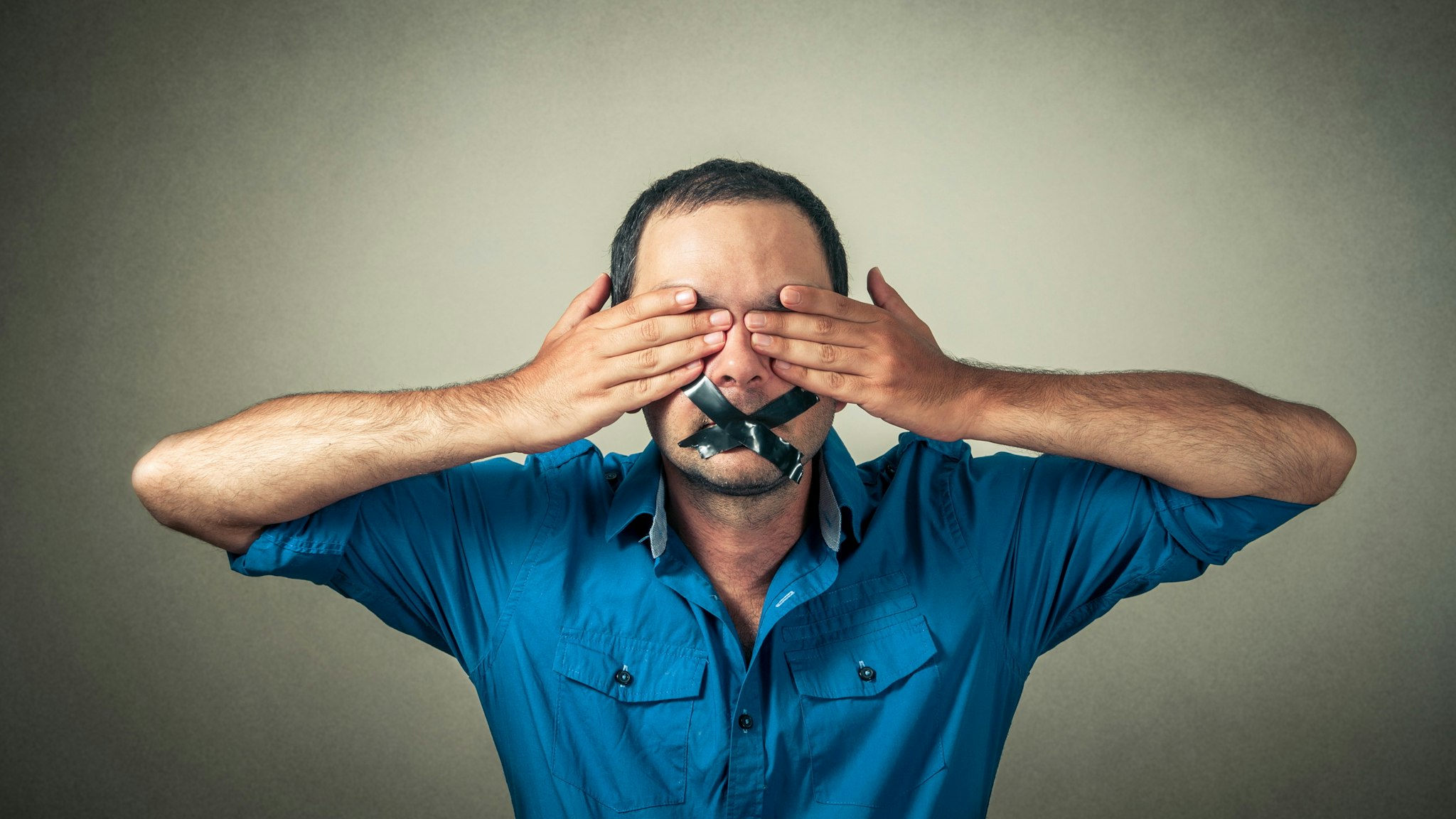 Portrait Of Scared Mid Adult Man With Black Adhesive Tape On Mouth Covering Eyes Against Gray Background - stock photo