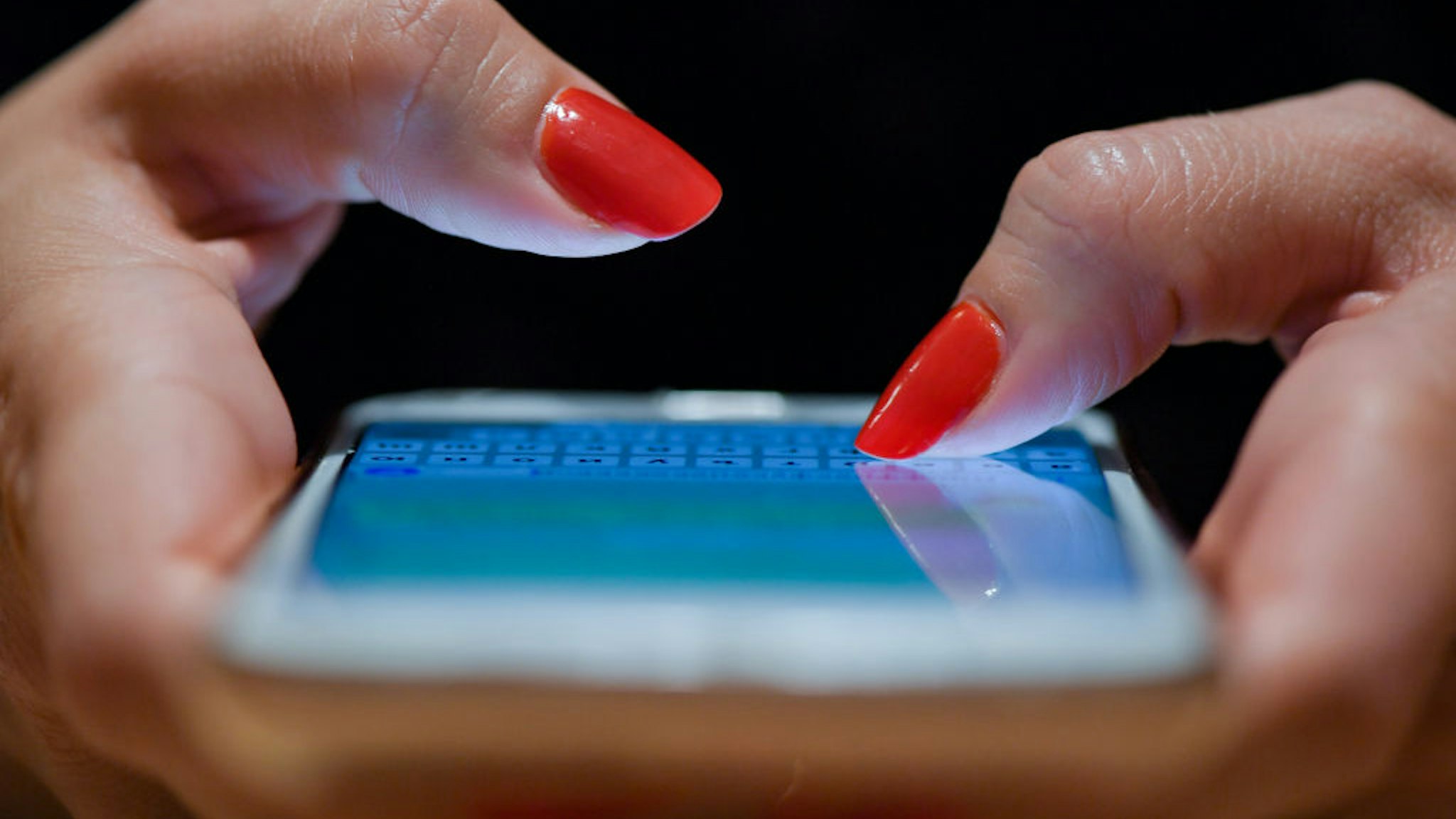 A woman with red fingernails writes a message on her smartphone.