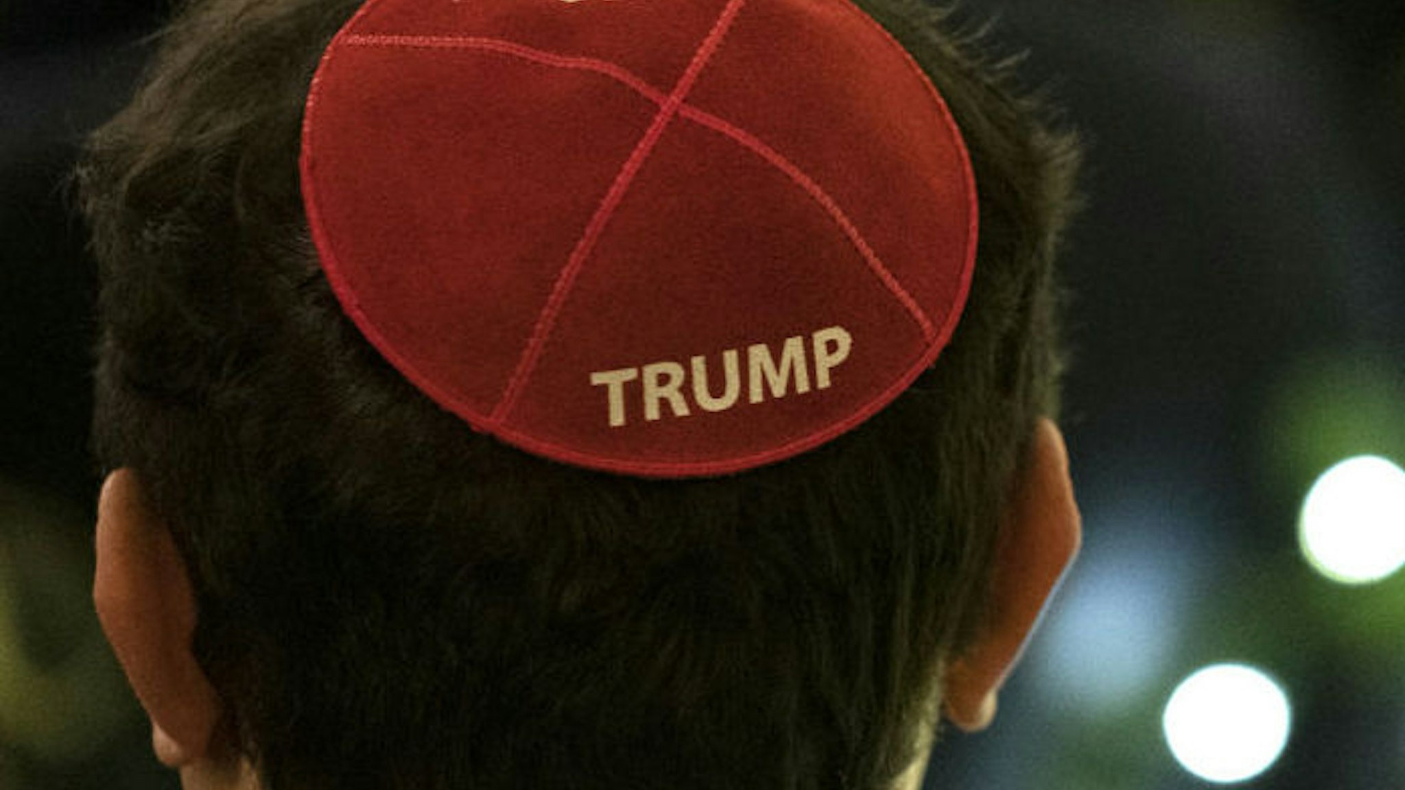 An attendee wears a Trump yarmulke as U.S. President Donald Trump speaks during a Hanukkah reception at the White House in Washington, D.C., U.S., on Wednesday, Dec. 11, 2019. During the event Trump signed an executive order stating that colleges and universities that allow groups with anti-Semitic beliefs to operate on their campuses will not receive federal educational funding.