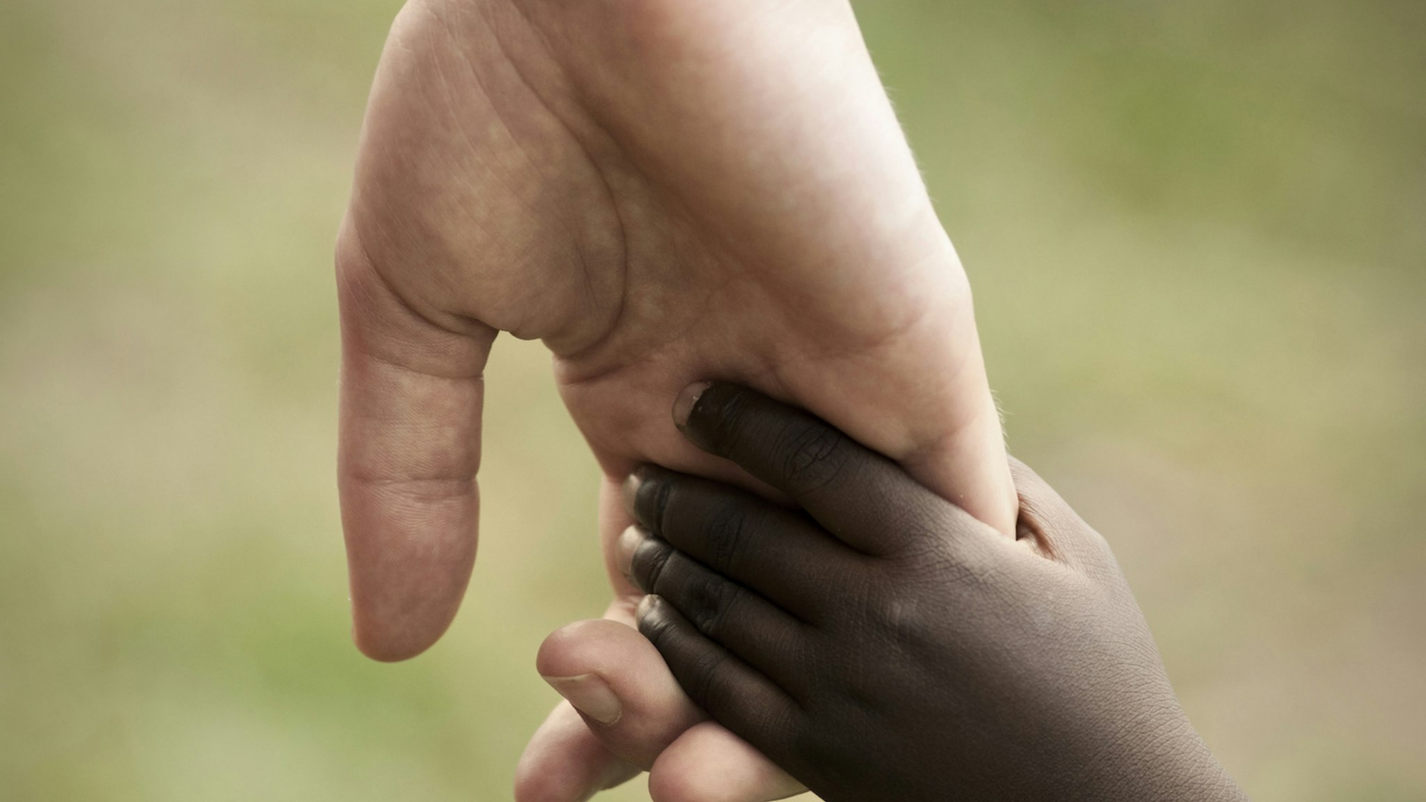 Hand of white adult and black child - stock photo