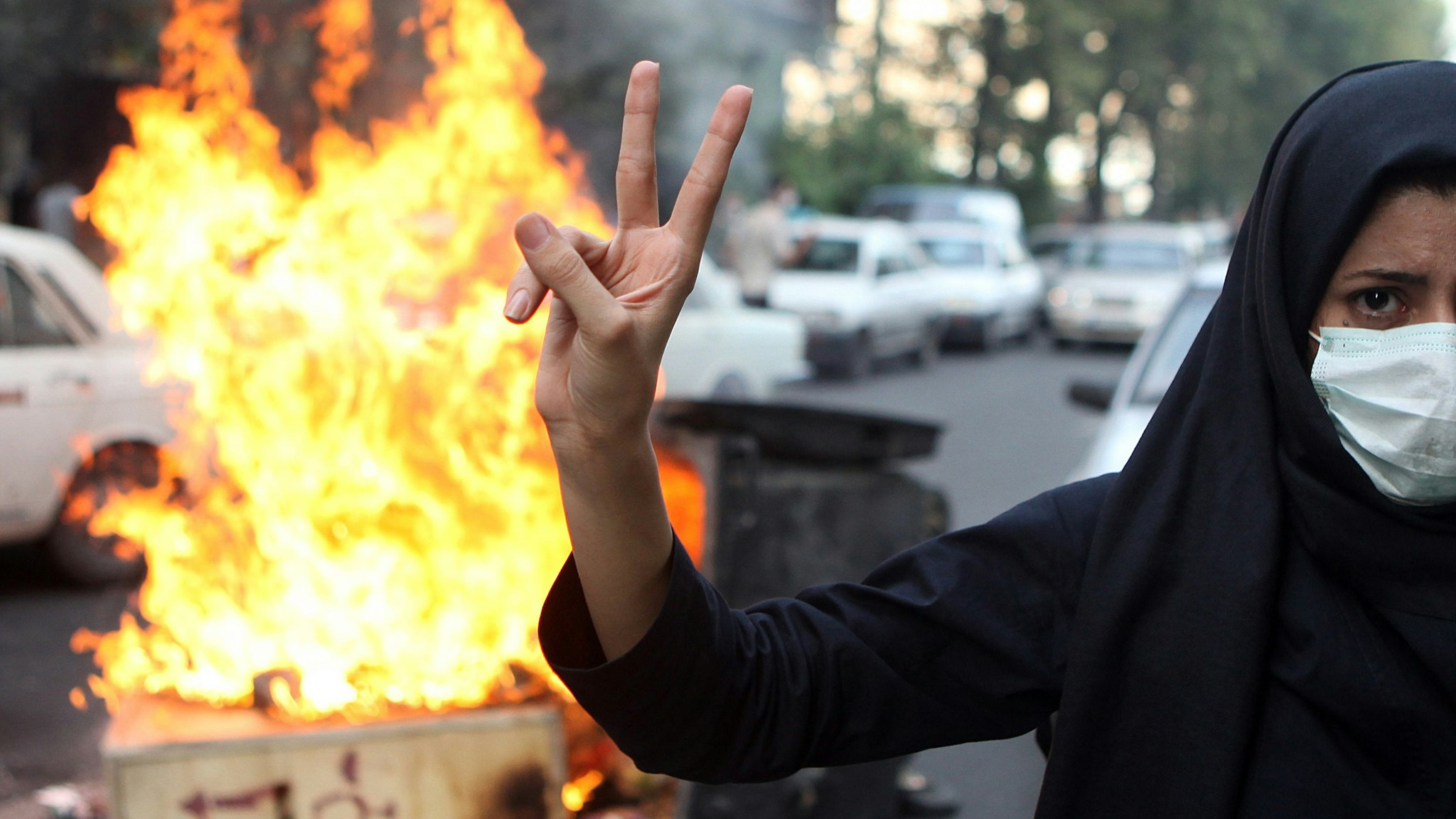 A woman protestor makes a V sign while standing in front of burning rubbish on July 9, 2009 in Tehran, Iran. Following recent unrest in the wake of the disputed presidental elections, demonstrators were met by force and tear gas rounds fired by Iranian police and Basij as they defied government warnings to stage a march in commeration of the anniversary of bloody student unrest at Tehran University in 1999.