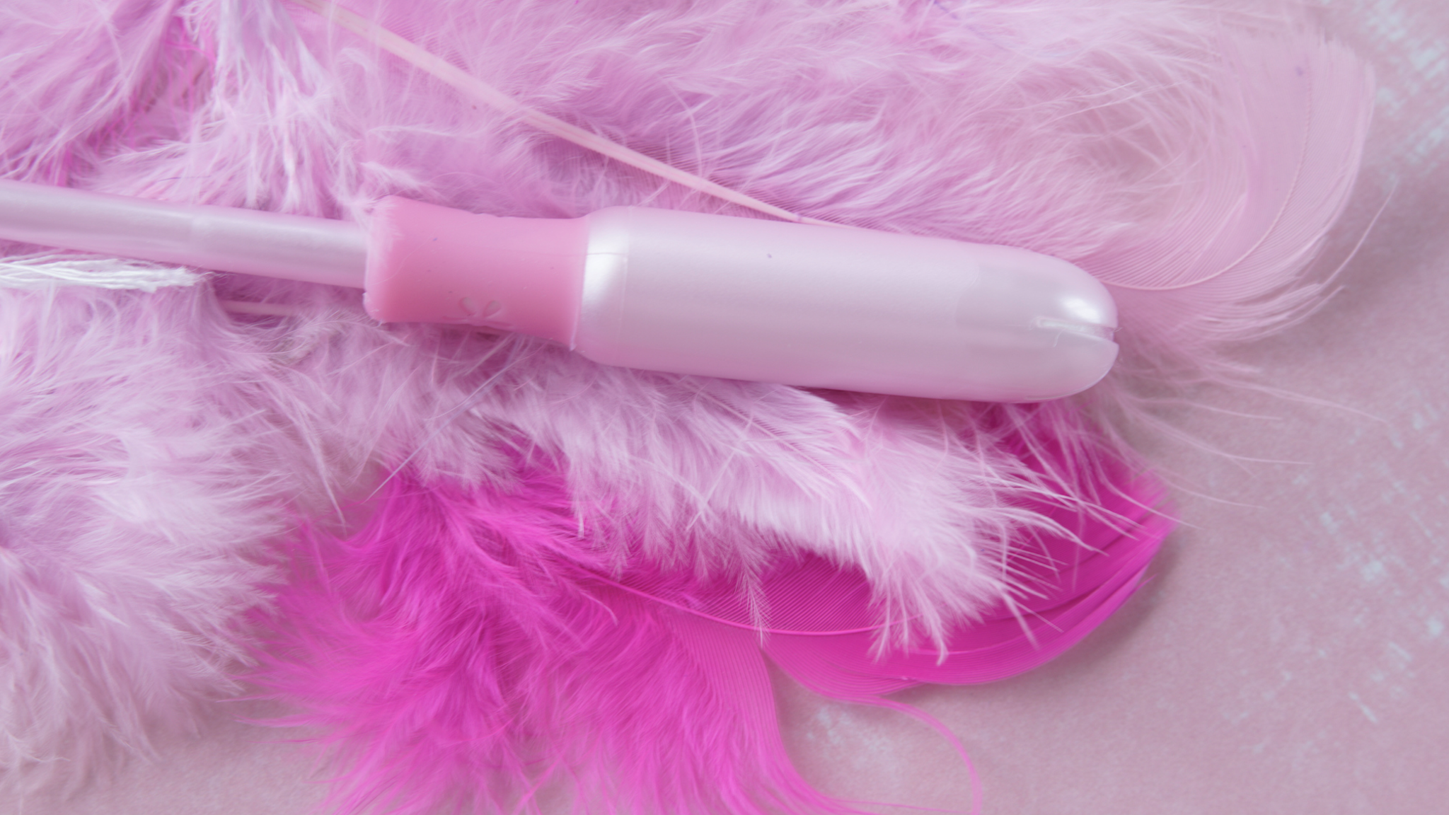 Modern menstruation. Still life of sanitary tampon with pink applicator with on a pink background withsoft pink feathers to give the conceptual idea of a light menstrual flow. Space for copy.