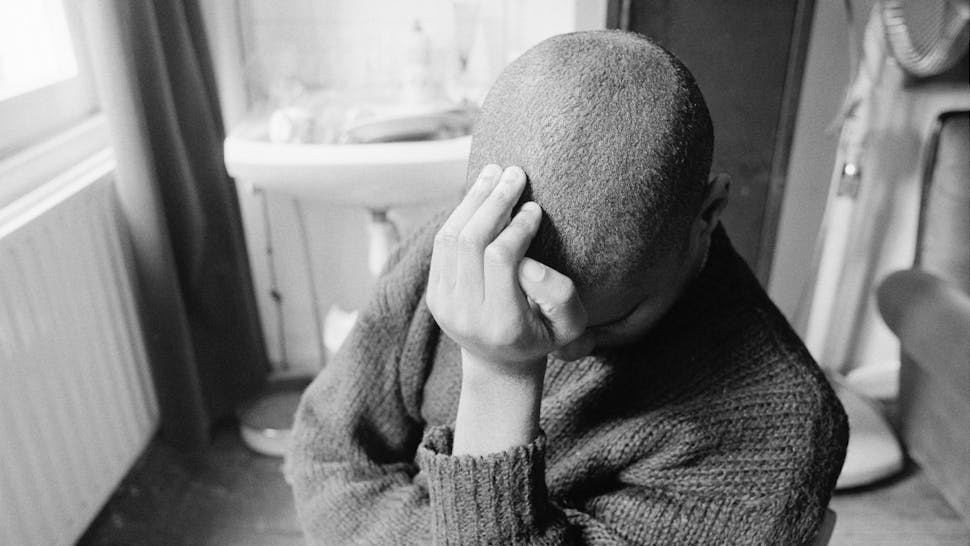 Depressed man. A man sitting alone in a room, leaning his head against the heel of his hand, circa 1985.