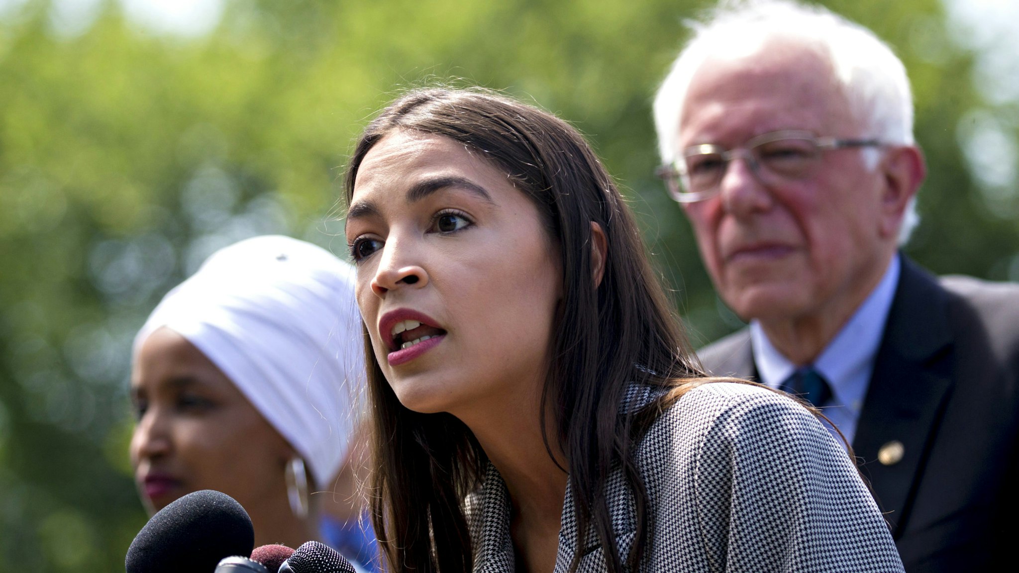 Representative Alexandria Ocasio-Cortez, a Democrat from New York, speaks as Senator Bernie Sanders, an independent from Vermont, right, and Representative Ilhan Omar, a Democrat from Minnesota, left, listen during a news conference announcing college affordability legislation on Capitol Hill in Washington, D.C., U.S., on Monday, June 24, 2019. Sanders is proposing to cancel the nation's outstanding $1.6 trillion of student debt and offsetting the cost with a tax on Wall Street transactions.