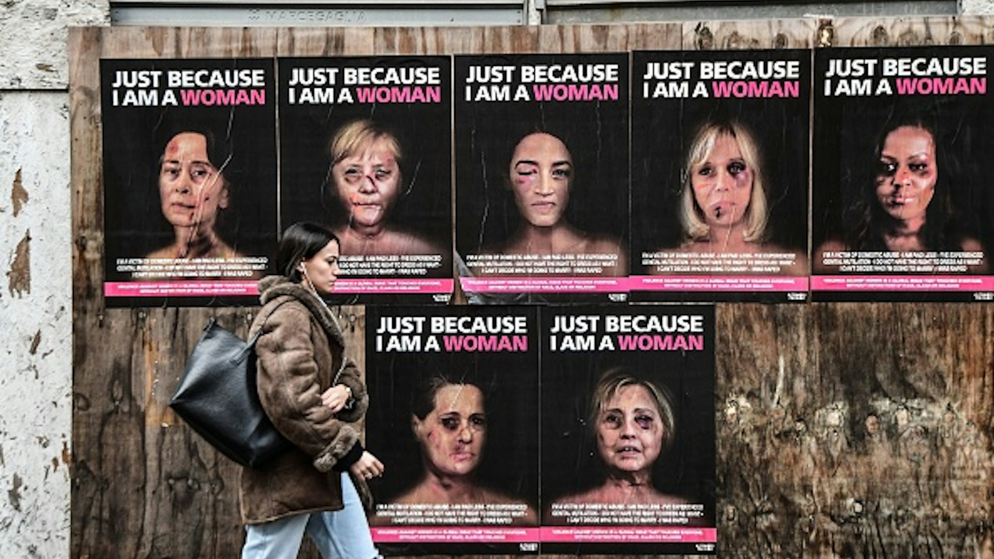 TOPSHOT - A woman walks past "Just because I am a Woman", a new series of works by Italian pop artist and activist aleXsandro Palombo, depicting some of the women protagonists of world politics as victims of gender violence : (Clockwise from Top L) Burmese politician Aung San Suu Kyi, German Chancellor Angela Merkel, member of the US House of Representatives Alexandria Ocasio-Cortez, the wife of the French president Brigitte Macron, former US First Lady Michelle Obama, former US First Lady and former US secretary of state Hillary Clinton and president of the Indian National Congress Sonia Gandhi, on January 15, 2020 in downtown Milan. - The series aims at raising awareness and get response from the institutions and the politics about domestic violence against women worldwide. (Photo by Miguel MEDINA / AFP) / RESTRICTED TO EDITORIAL USE - MANDATORY MENTION OF THE ARTIST UPON PUBLICATION - TO ILLUSTRATE THE EVENT AS SPECIFIED IN THE CAPTION
