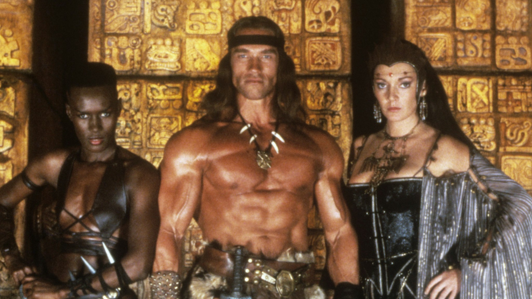 Austrian-born American actor, producer and politician Arnold Schwarzenegger, Jamaican singer, actress and model Grace Jones and British actress Sarah Douglas looking into the camera in the film Conan the Destroyer. Mexico, 1984 (Photo by Mondadori via Getty Images)