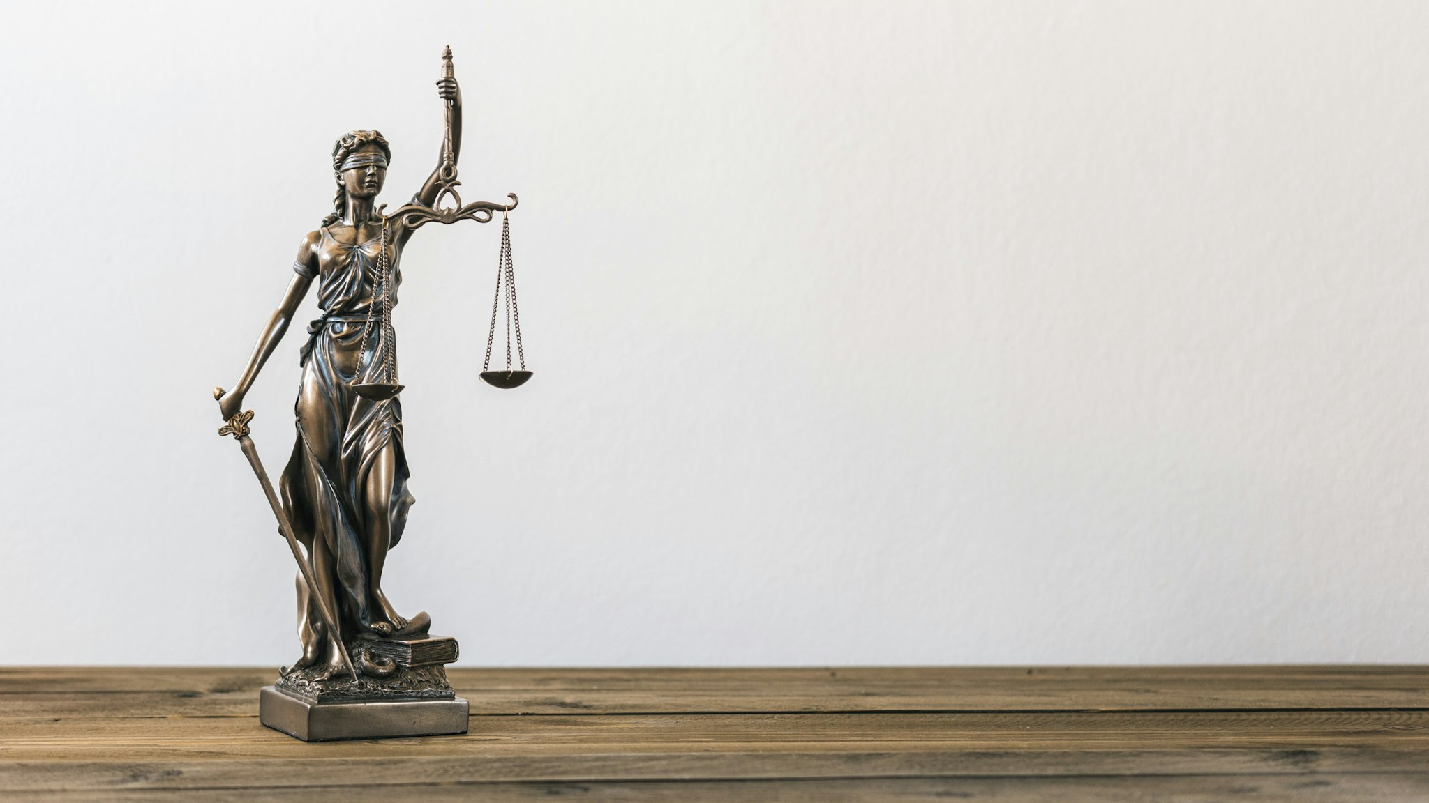 Close-Up Of Lady Justice On Table Against Wall - stock photo